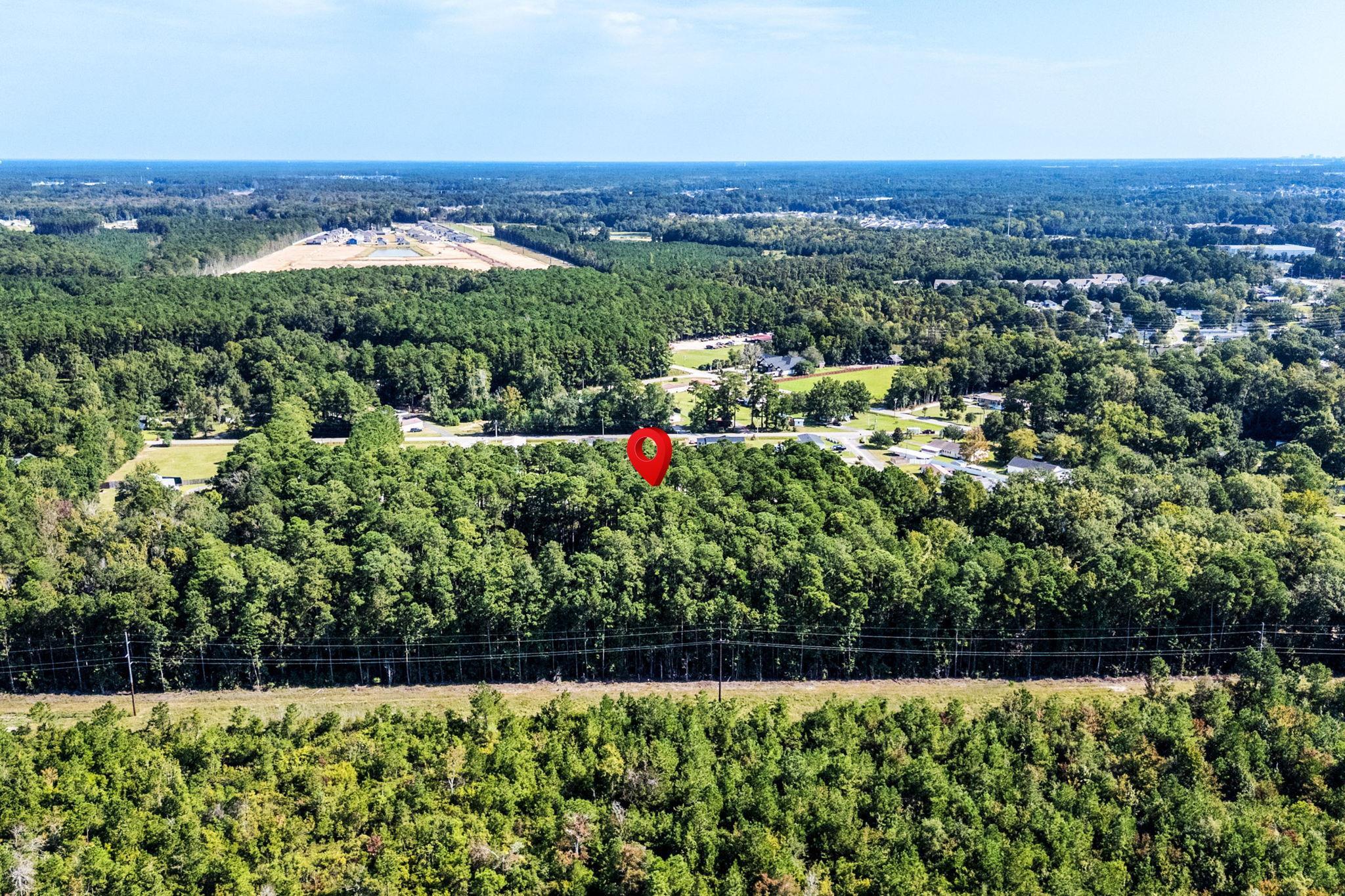 Aerial view of wooded property marked by a red pin, with surrounding forest and nearby homes.