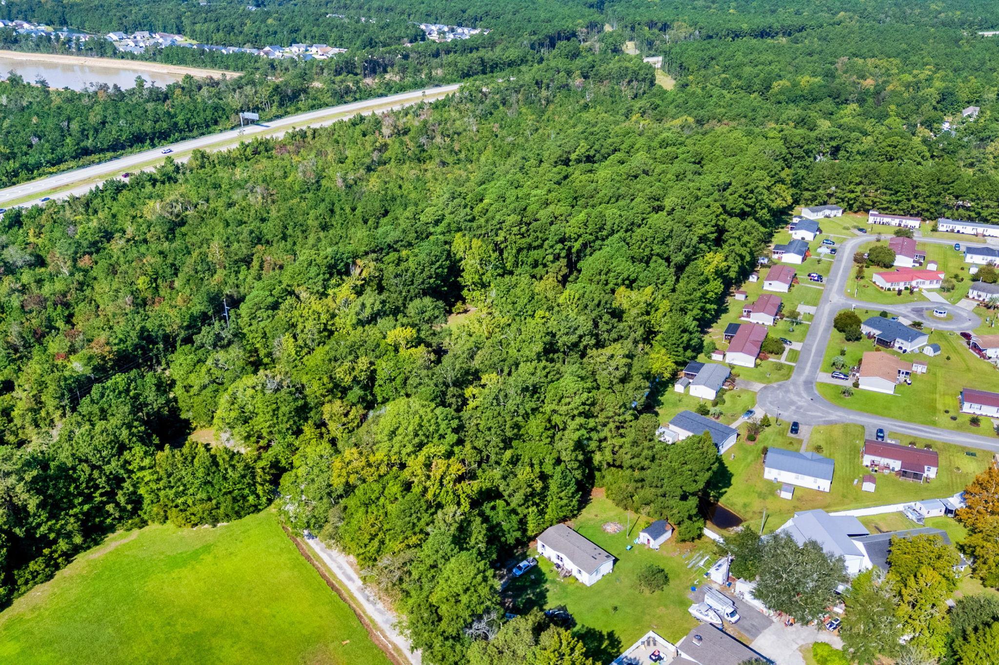 Aerial view of dense woodland beside homes, a highway, and an open grassy area.