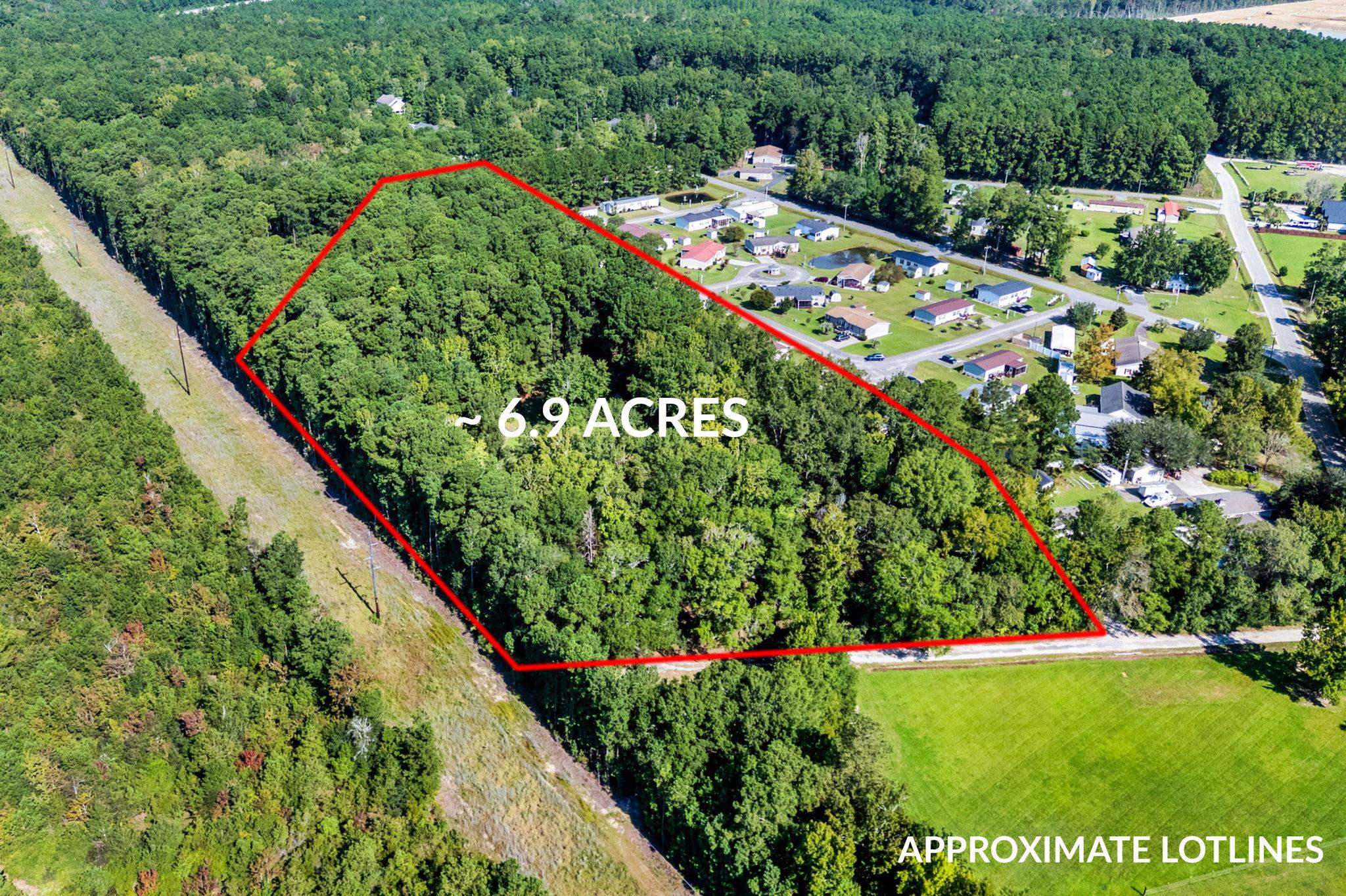 Aerial view of a wooded 6.9-acre parcel outlined in red beside a residential neighborhood.