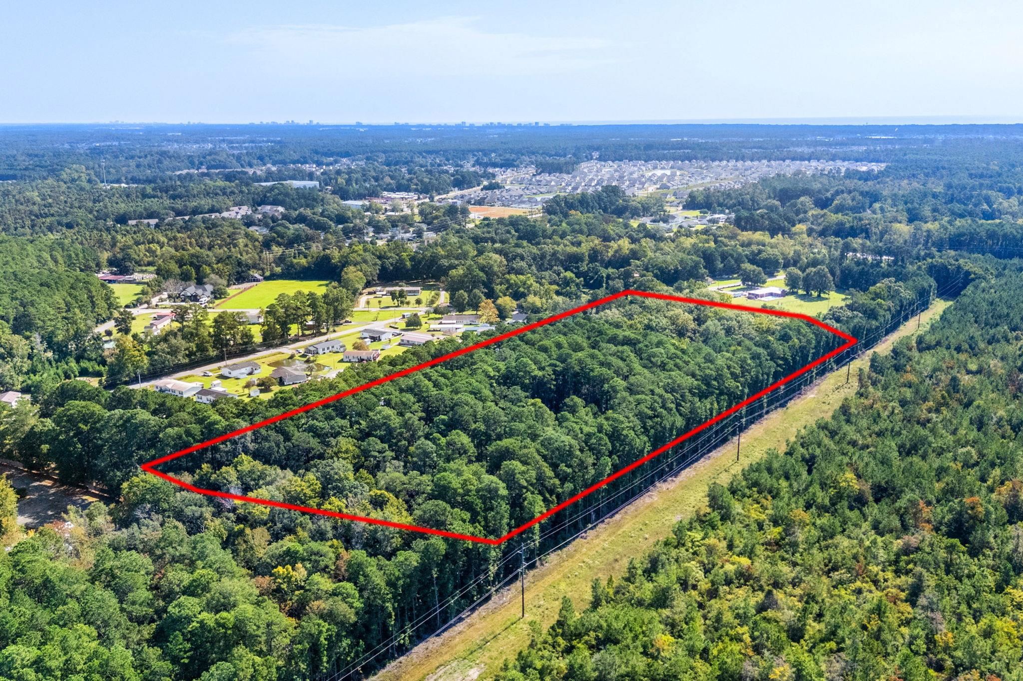 Aerial view of a wooded parcel outlined in red beside a utility corridor and nearby homes.