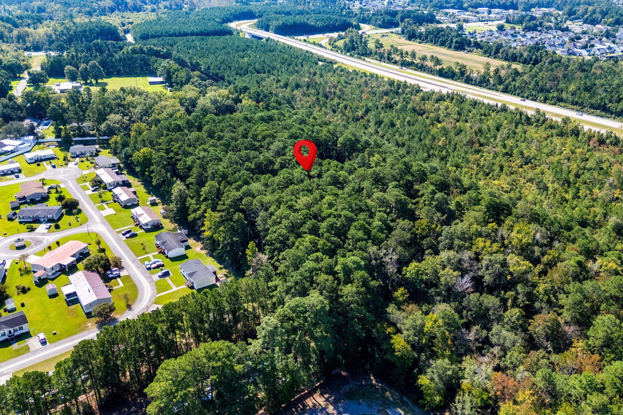 Aerial view of a wooded parcel marked by a red pin beside a residential neighborhood.
