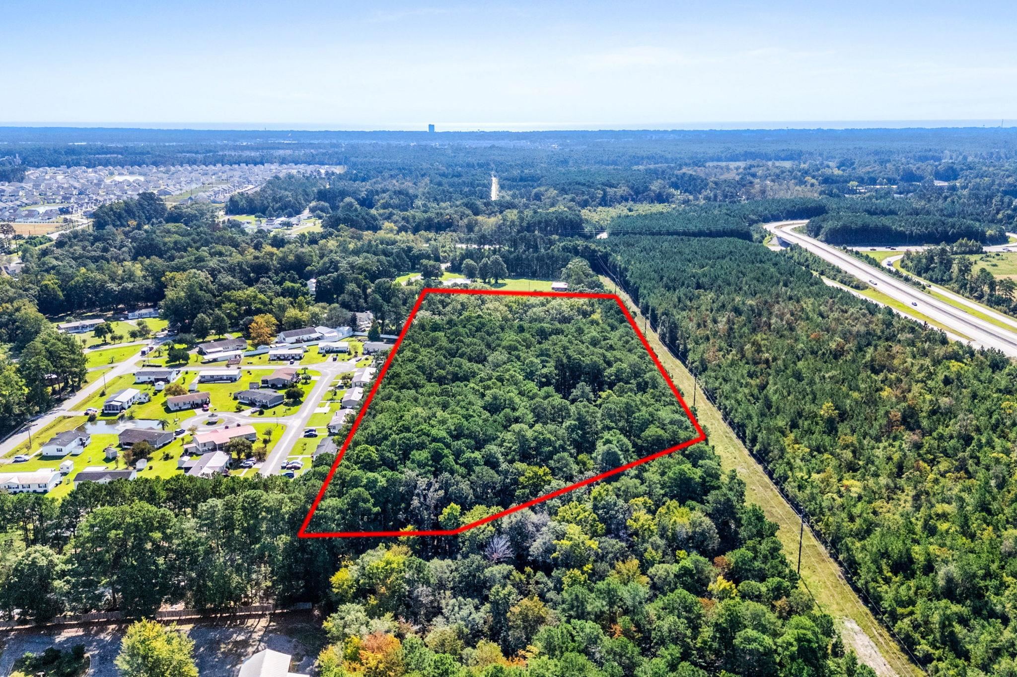 Aerial view of a densely wooded parcel outlined in red beside homes and a highway.