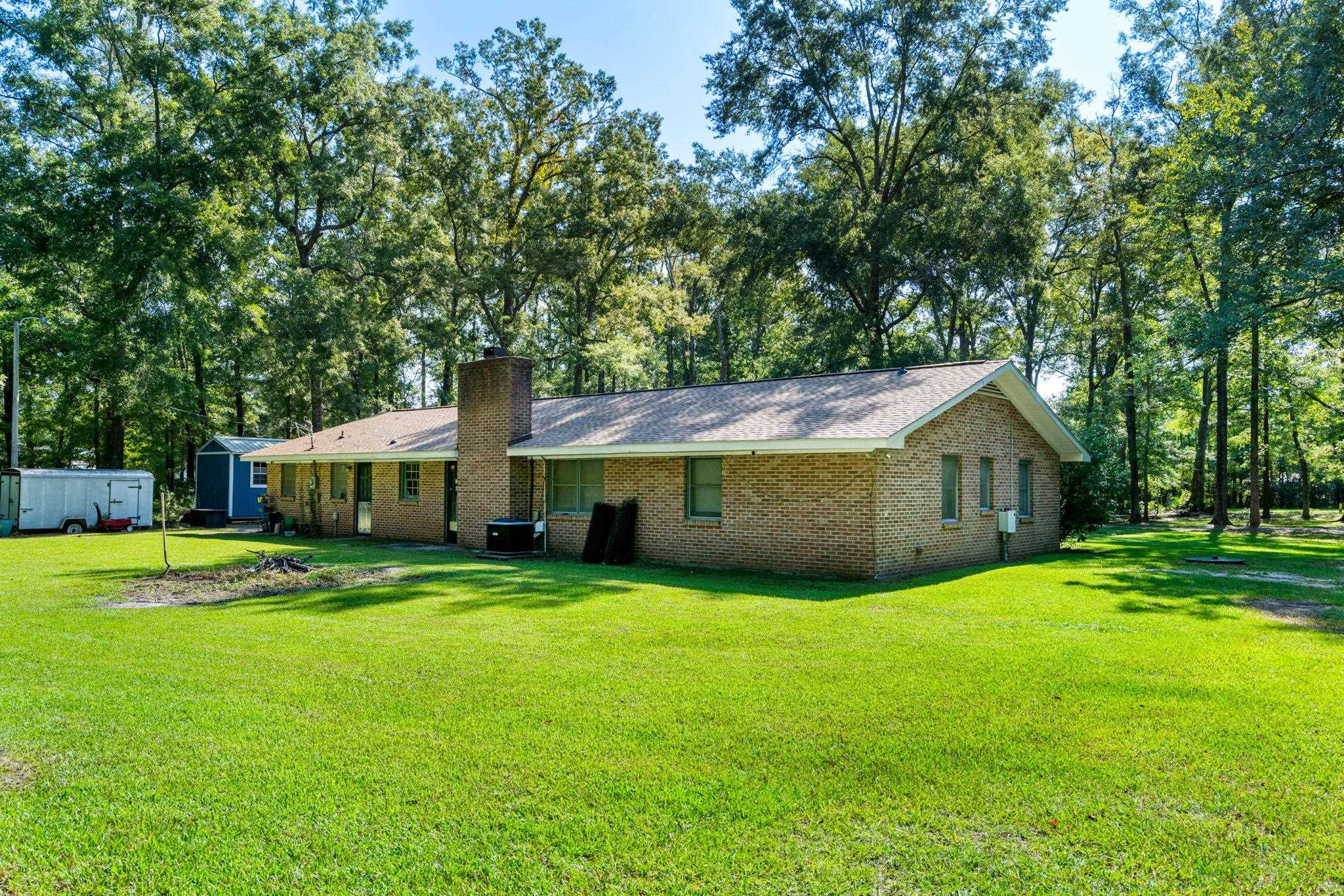 Brick ranch house with a chimney, broad green lawn, and mature trees.