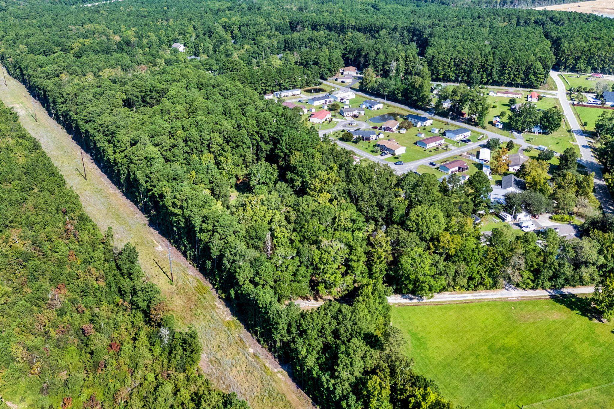 Aerial view of dense woodland beside homes and an open field, with a cleared utility corridor.