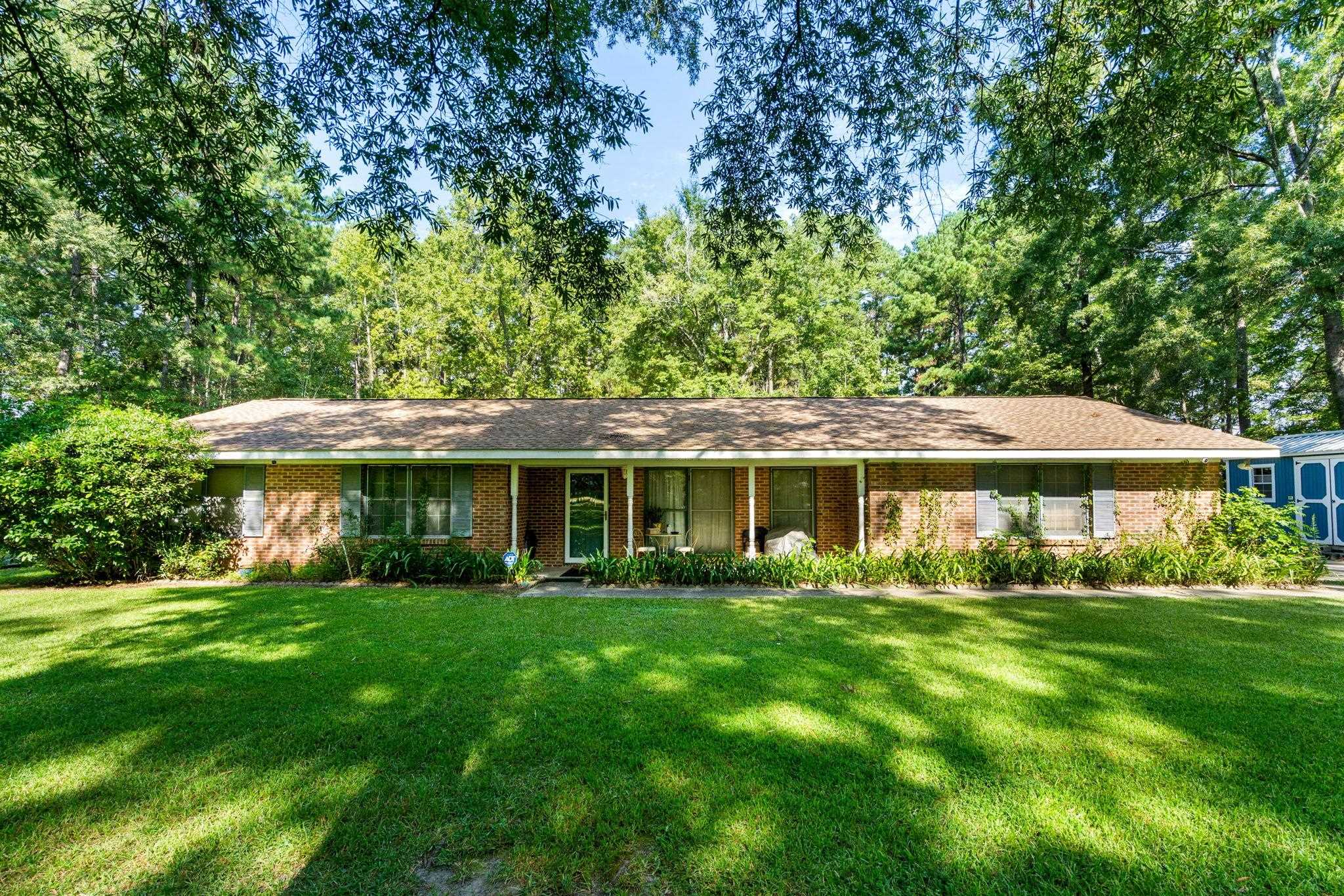 Single-story brick ranch home with a covered porch, broad lawn, and mature trees.