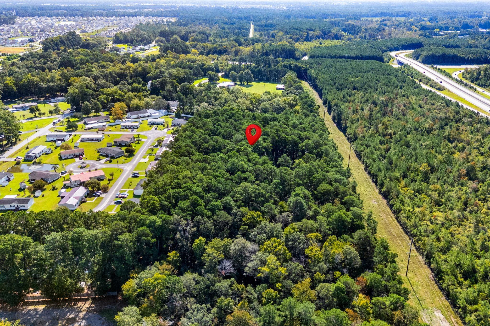 Aerial view of a wooded property marked by a red pin beside homes and a highway.