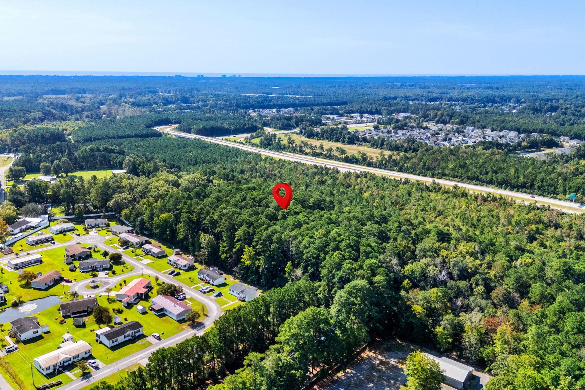 Aerial view of a wooded property marked by a red pin, near homes and a highway.