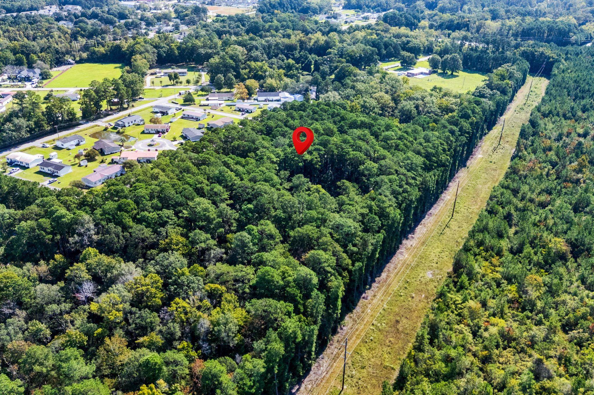 Aerial view of a wooded parcel marked by a red pin beside a cleared utility corridor and nearby homes.