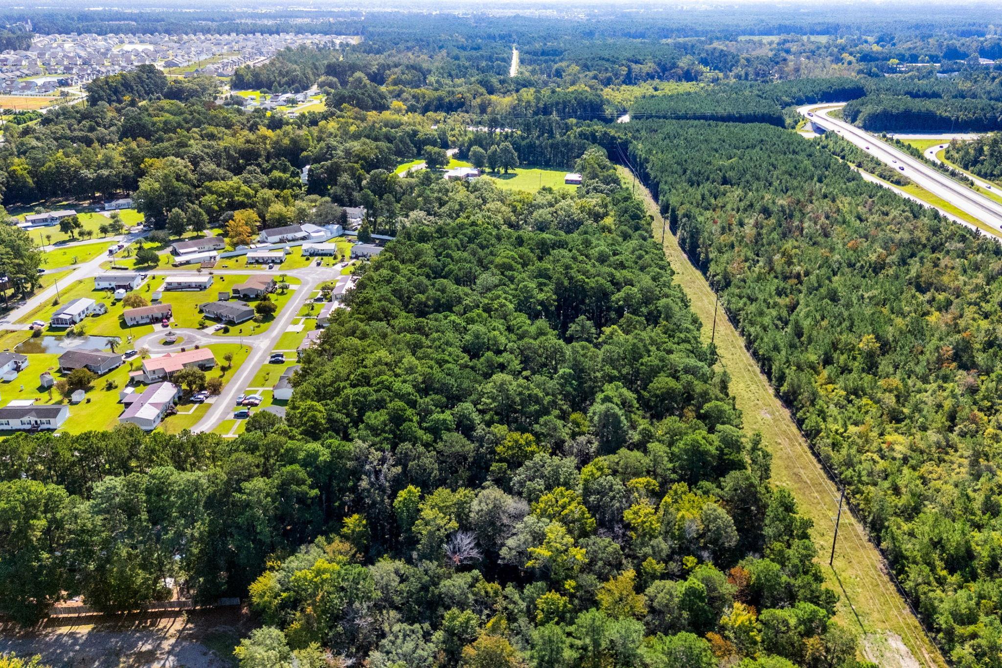 Aerial view of wooded land beside a neighborhood, highway, and power-line corridor.