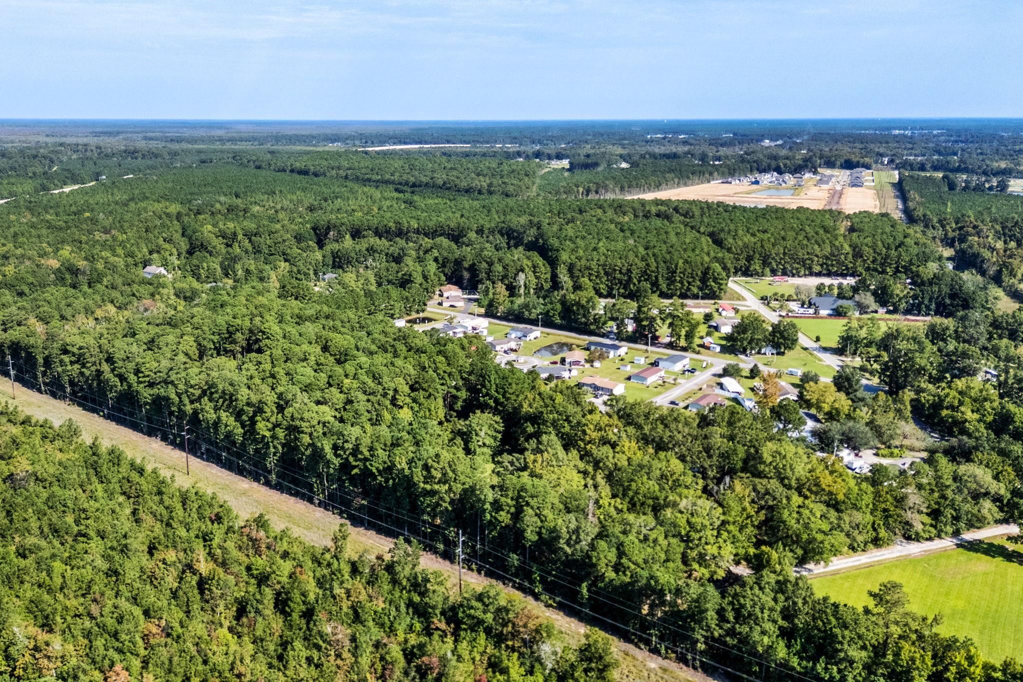 Aerial view of wooded land surrounding a small neighborhood, with utility lines crossing the foreground.