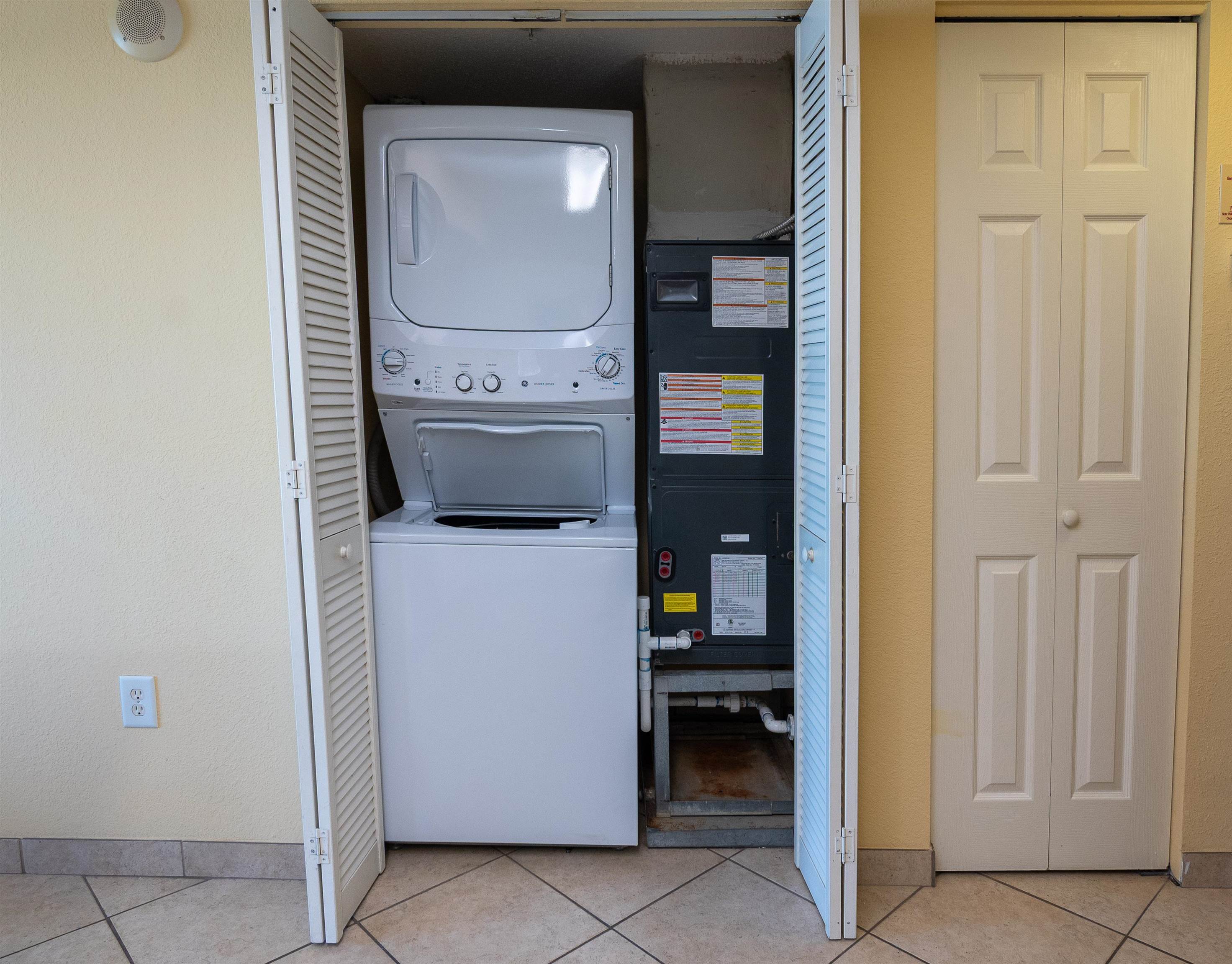 Open laundry closet with a stacked washer and dryer beside the HVAC unit.