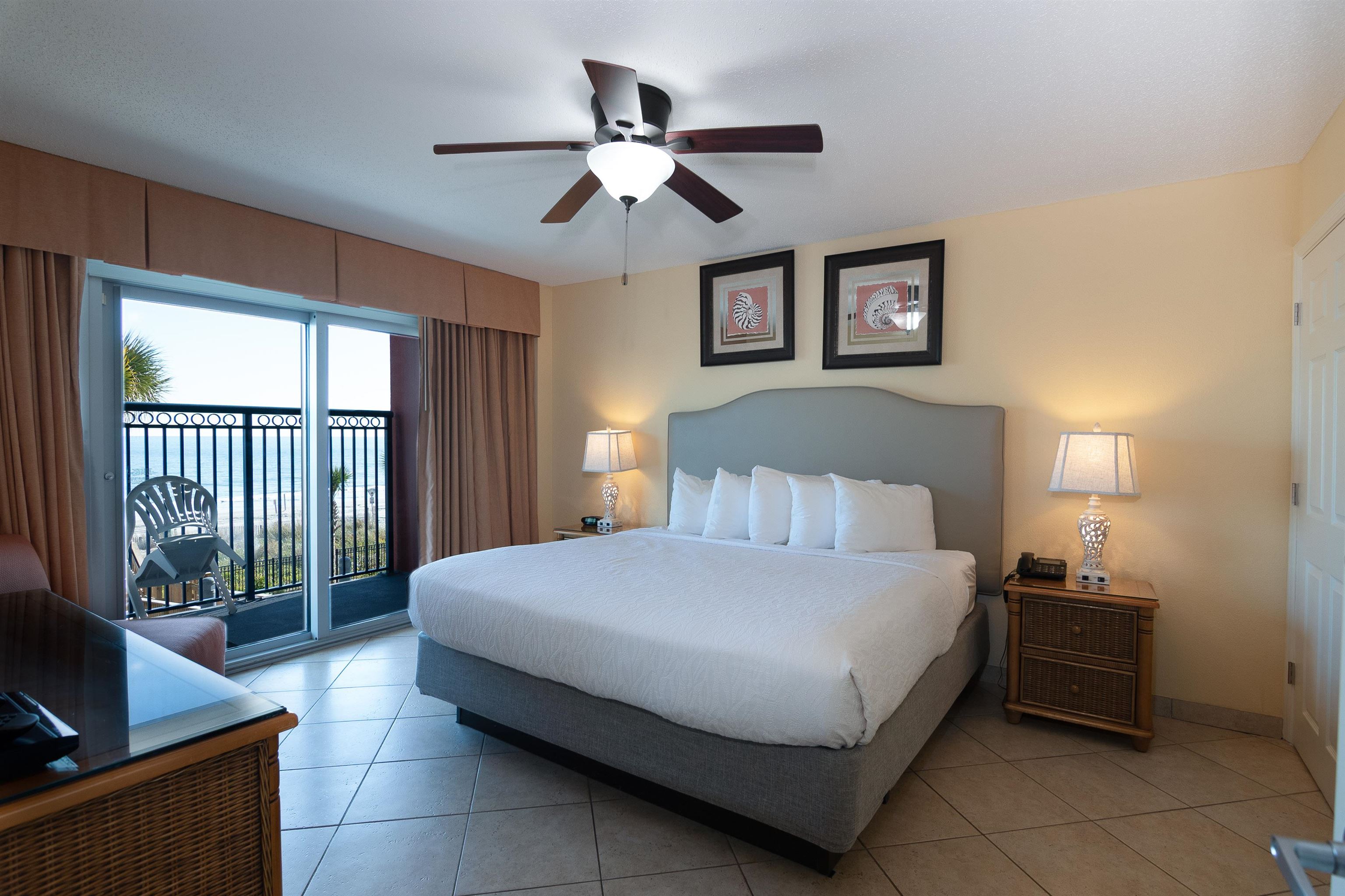 Furnished bedroom with a king-size bed and sliding doors overlooking the ocean from a balcony.