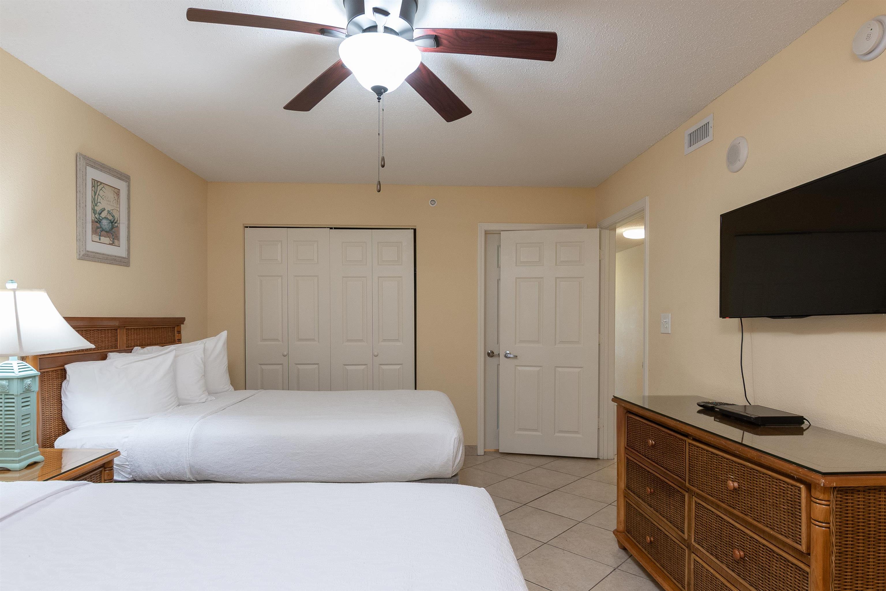 Furnished bedroom with two white beds, a ceiling fan, and a wall-mounted television.