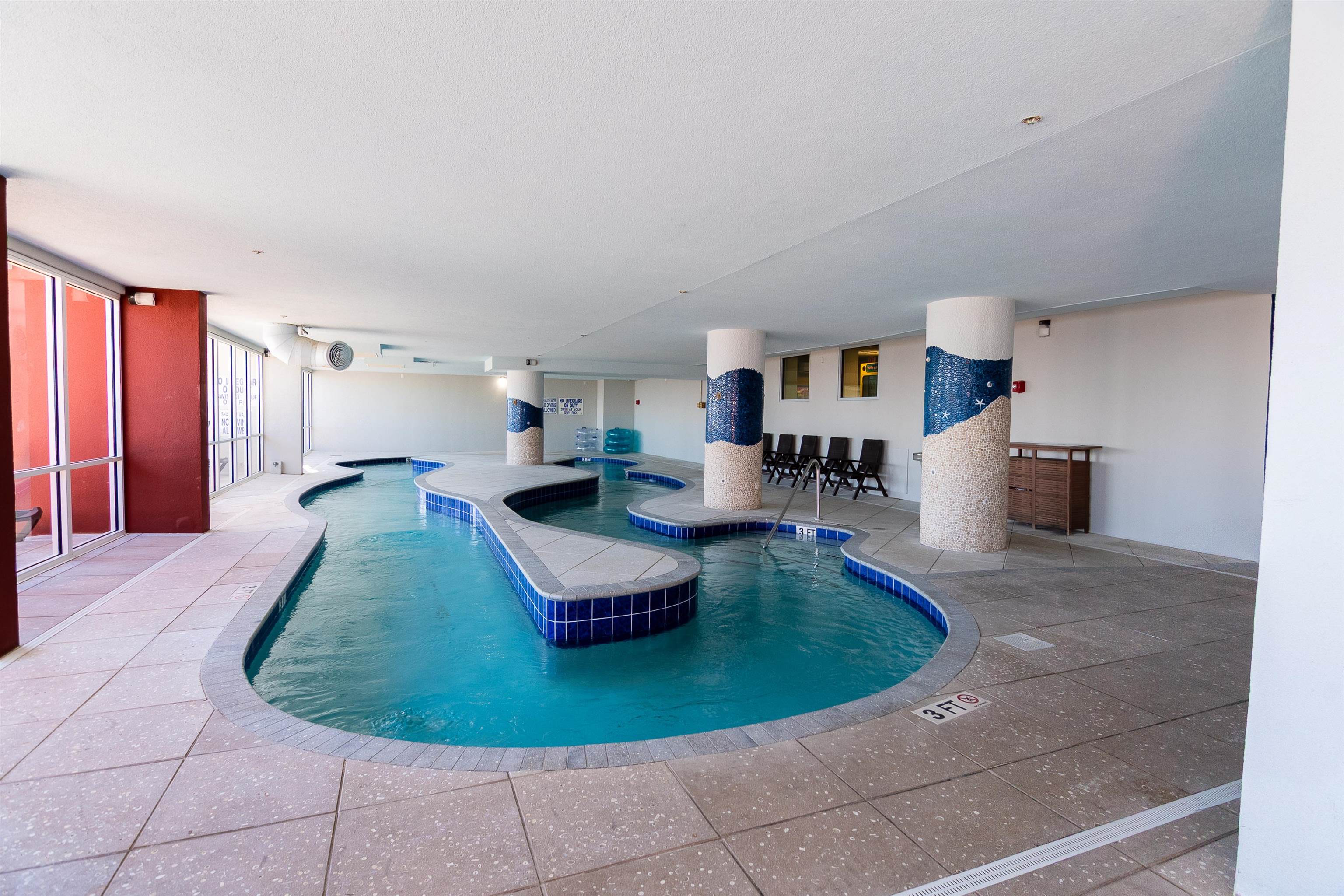 Indoor pool with winding blue-tiled edges, mosaic columns, and lounge chairs.