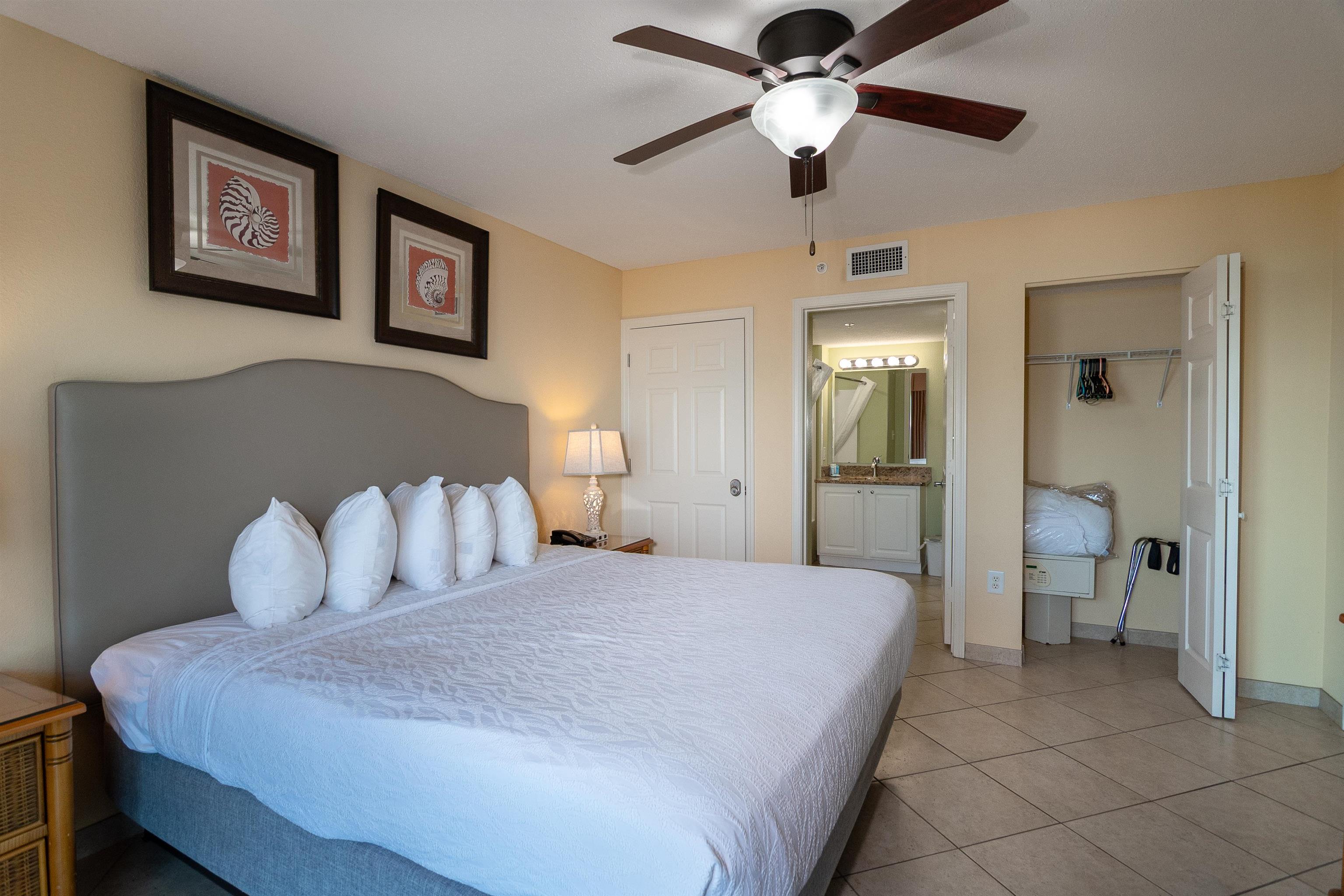 Furnished bedroom with a large bed, ceiling fan, and open doors to the bathroom and closet.
