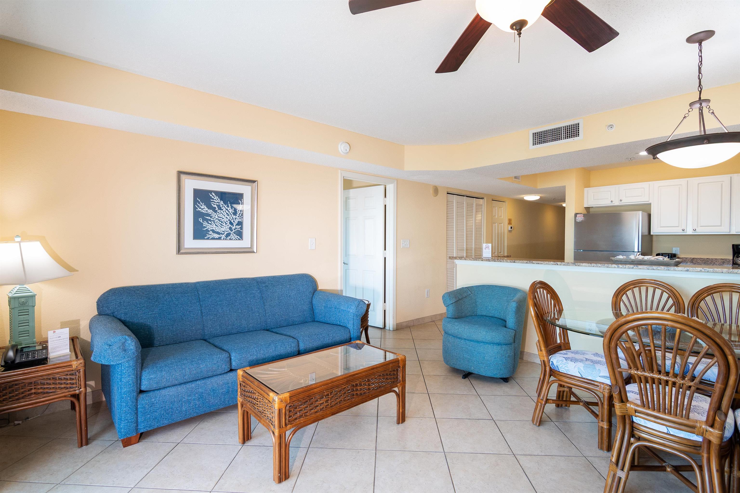 Condo living and dining area with blue seating, wicker furniture, and an open kitchen.