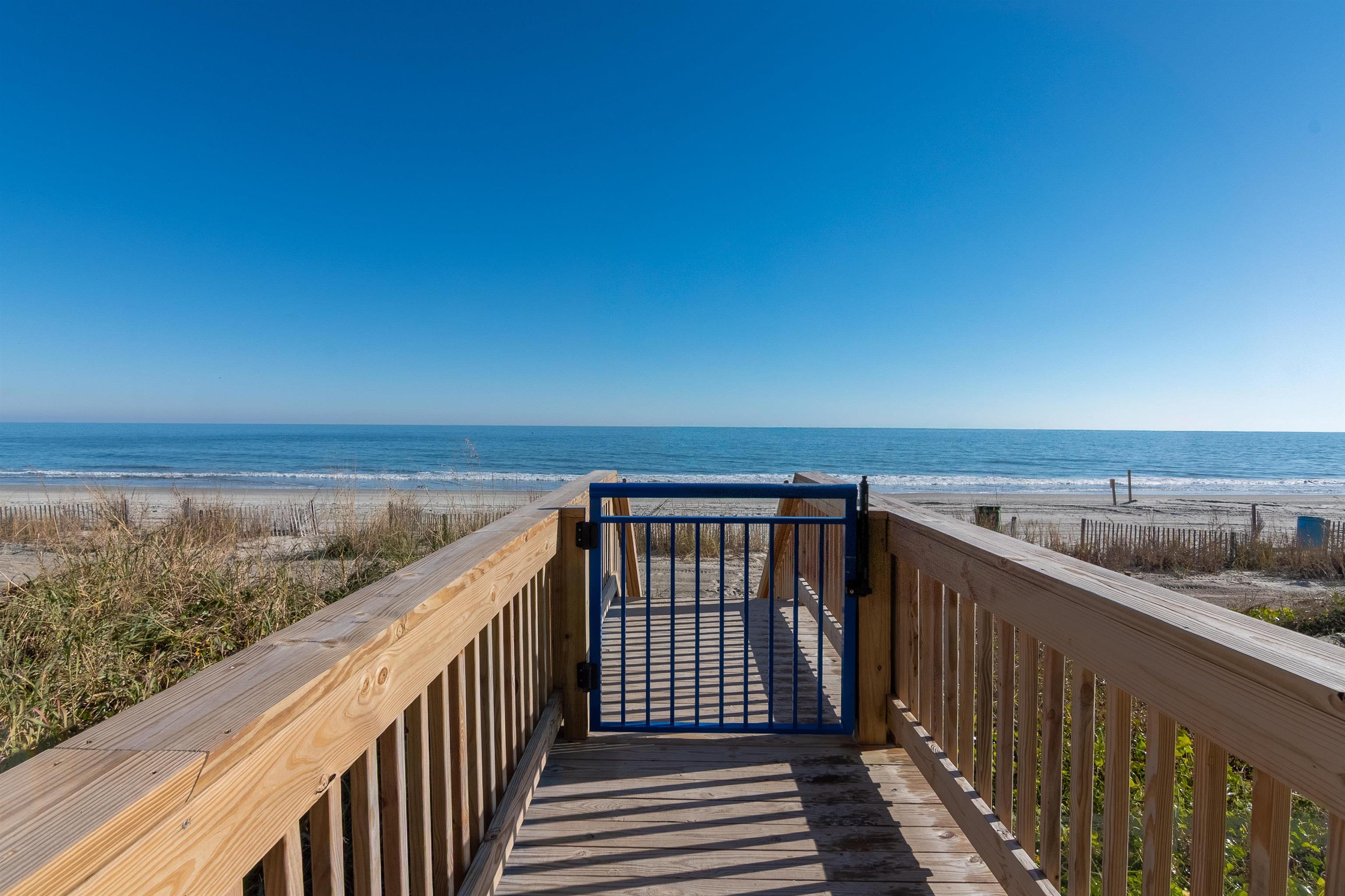 Wooden beach access walkway and blue gate leading to a sandy beach and ocean.