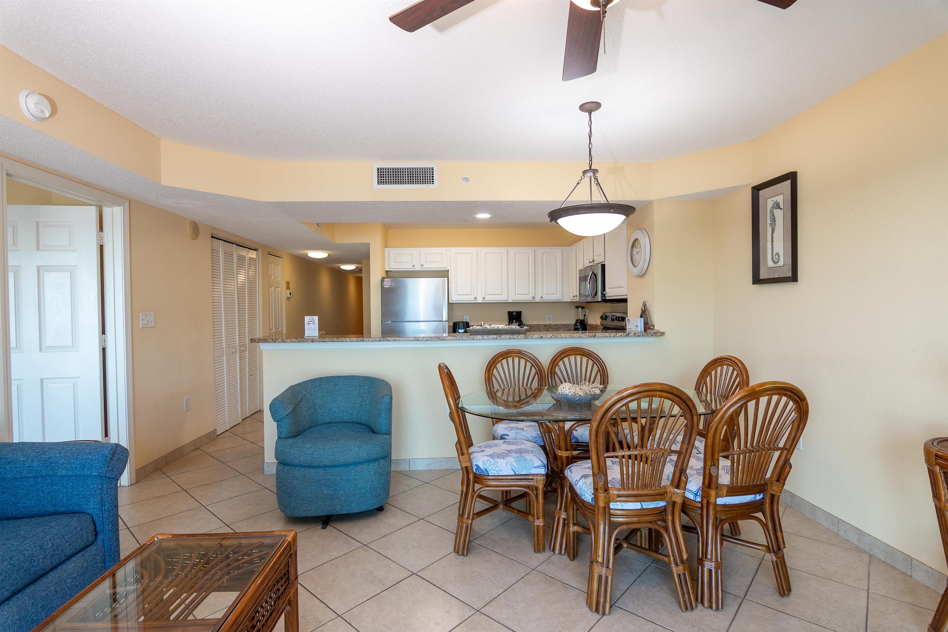 Open kitchen and dining area with a breakfast bar, rattan chairs, and blue living room seating.