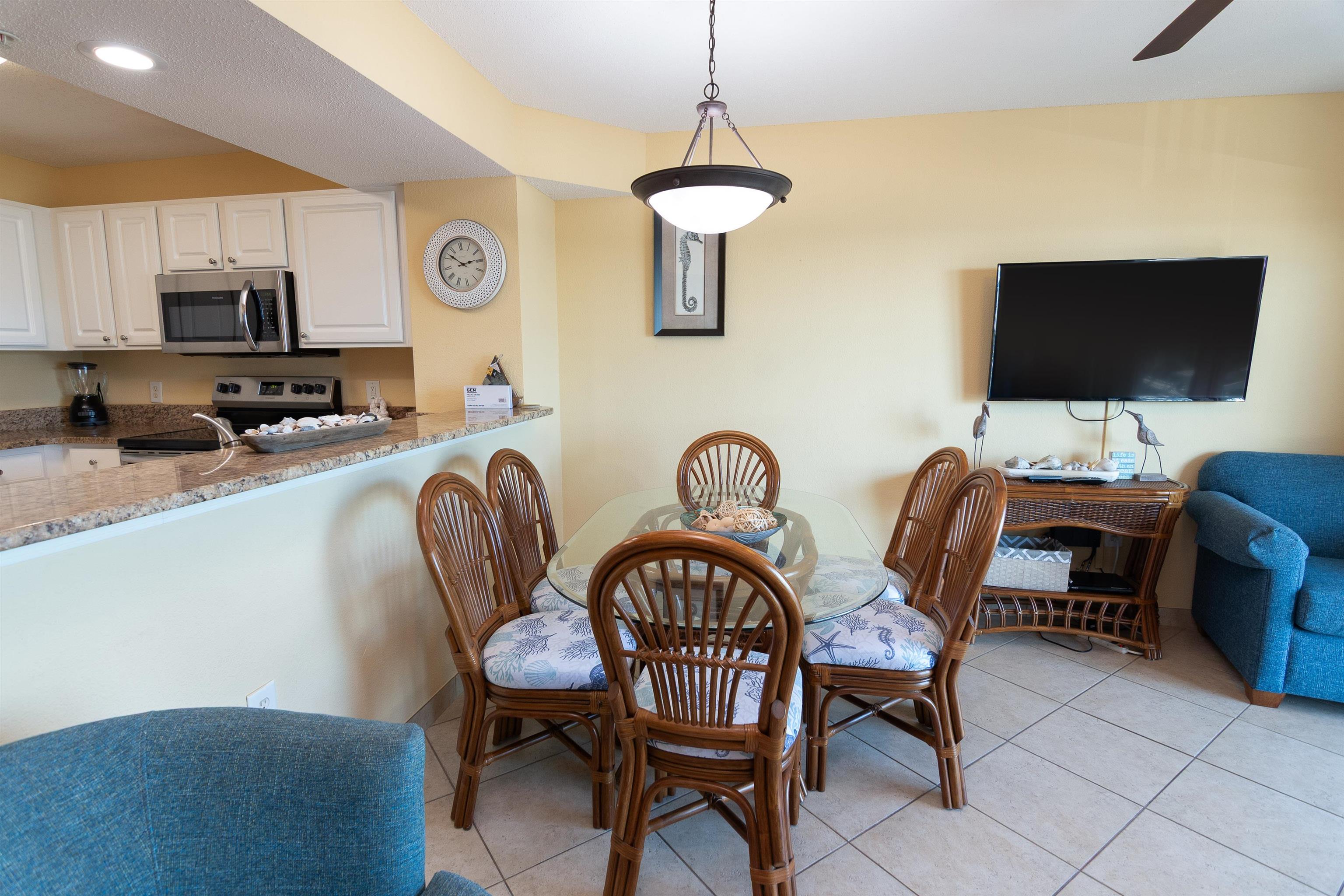 Dining area with wicker chairs, a glass-top table, and an open kitchen with granite breakfast bar.