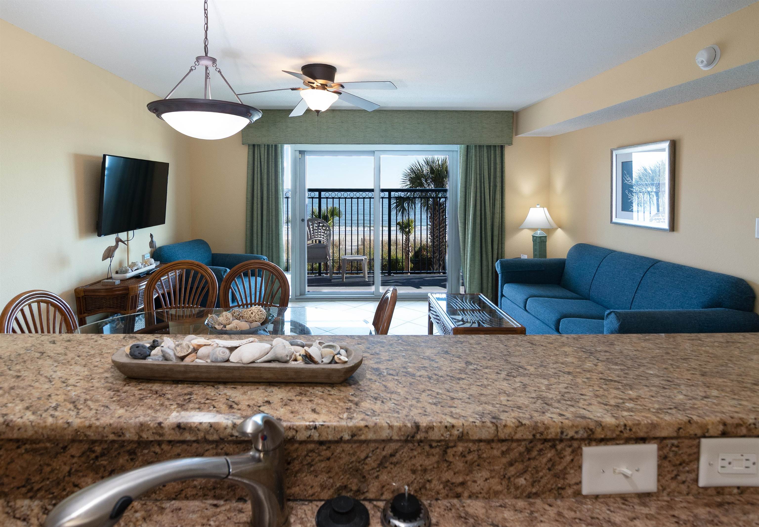 Living and dining area with blue sofas and sliding doors opening to an ocean-view balcony.