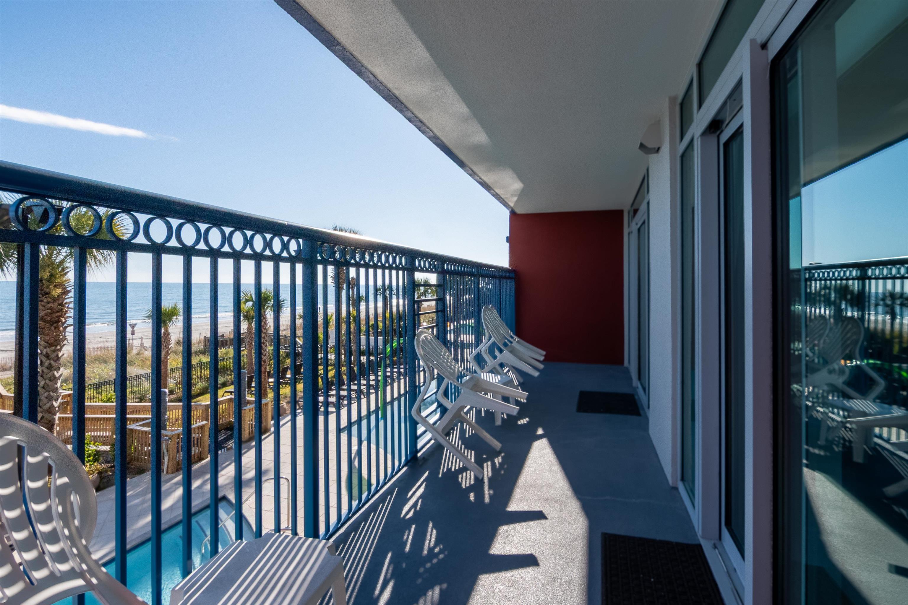 Condominium balcony with white chairs overlooking the beach and ocean.