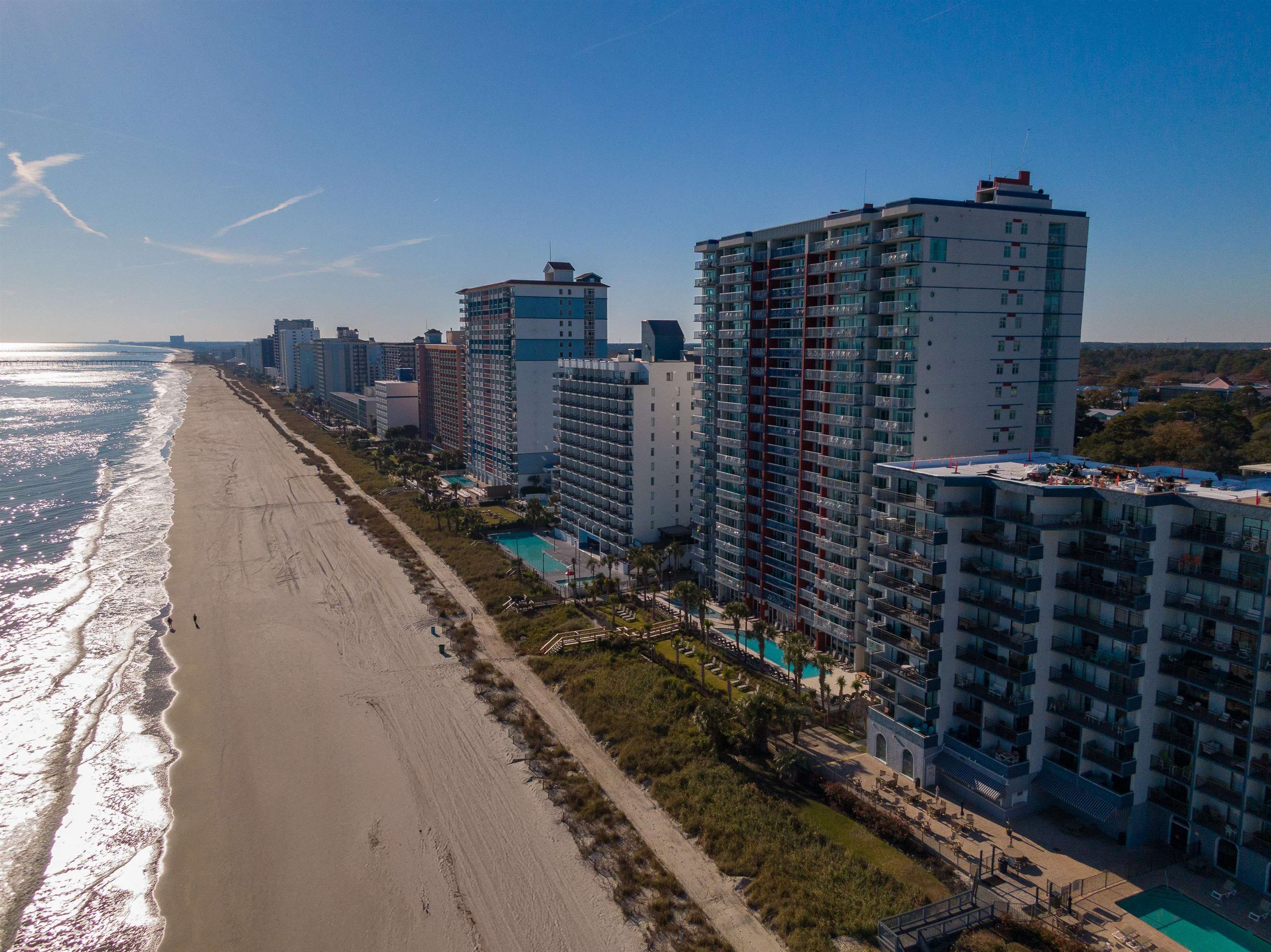 Beachfront condominiums line the sandy shore beside the ocean, with outdoor pools below.