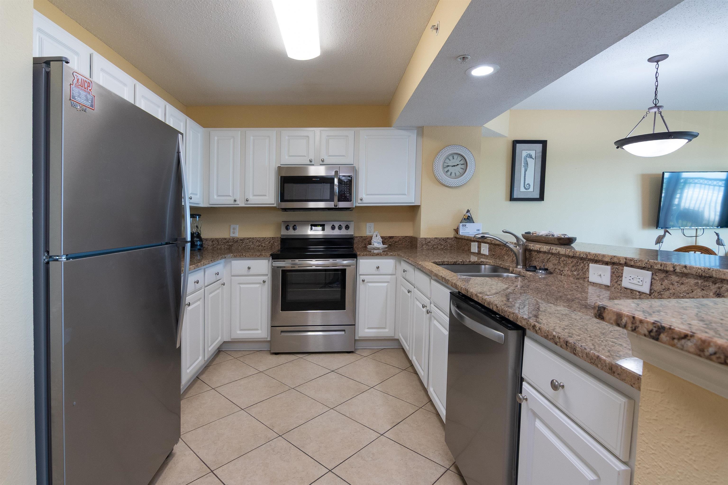Condominium kitchen with white cabinets, stainless steel appliances, and brown granite counters.