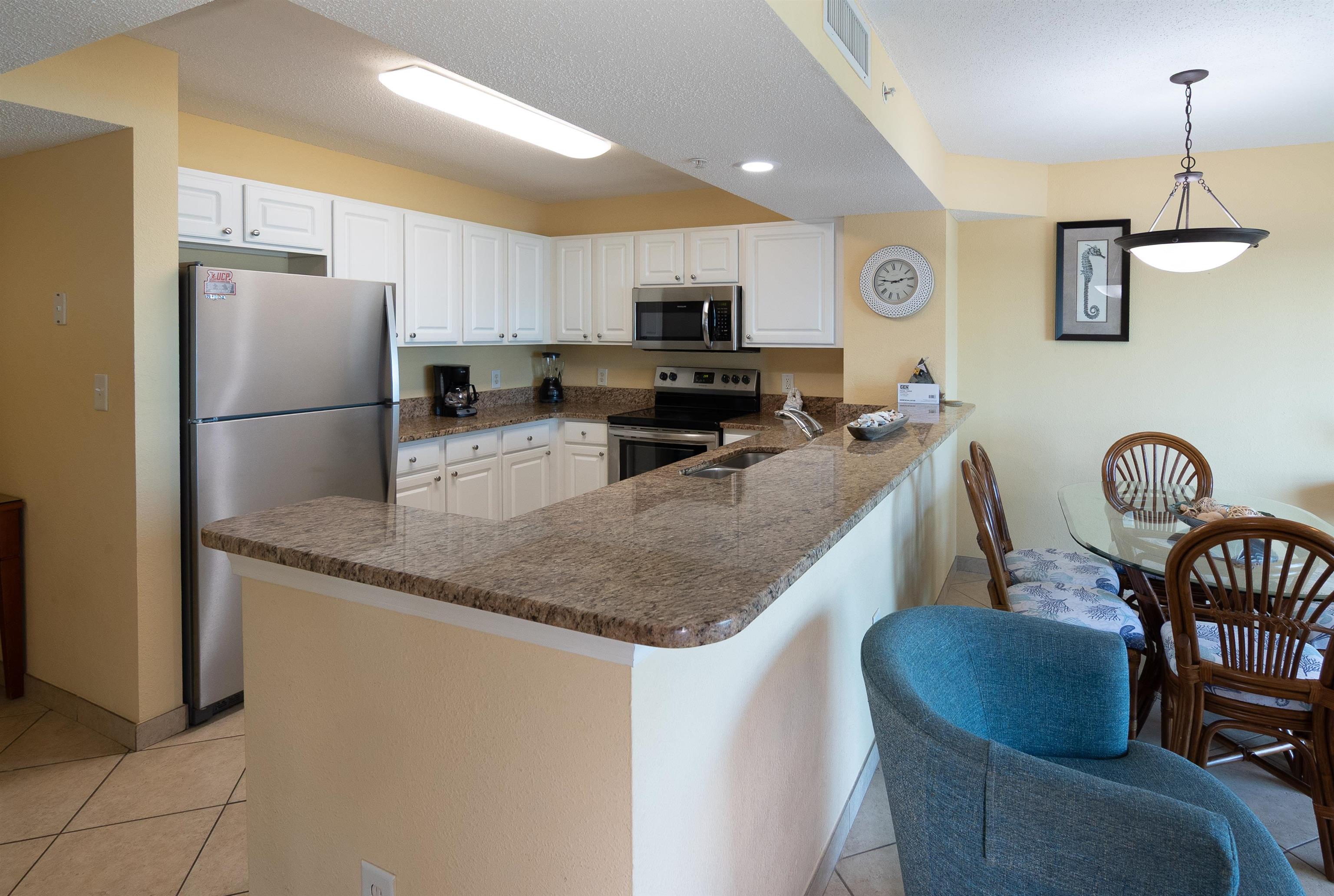 Condo kitchen with granite breakfast bar, white cabinets, stainless appliances, and an adjoining dining area.