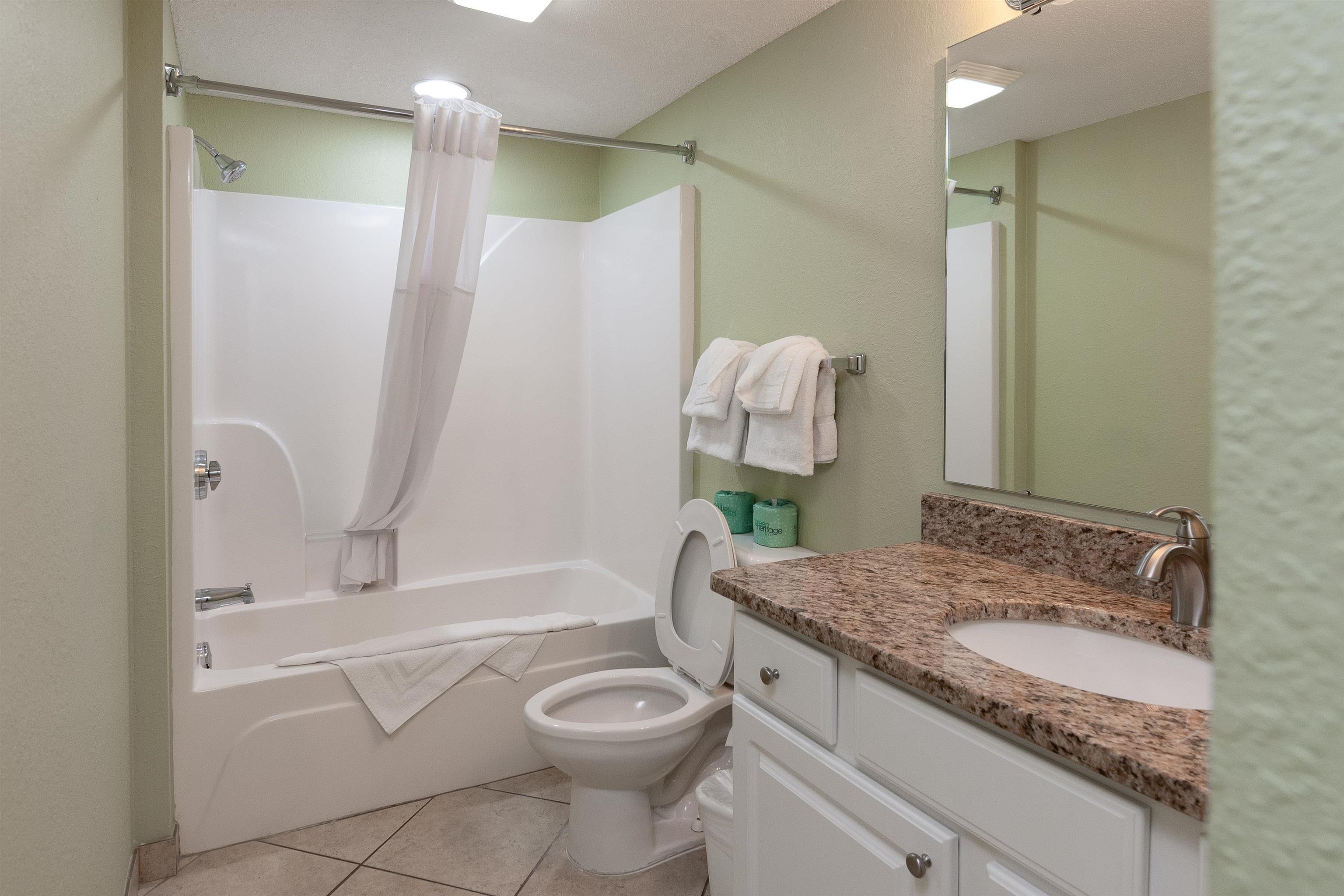 Bathroom with a white tub, toilet, and granite-topped vanity.