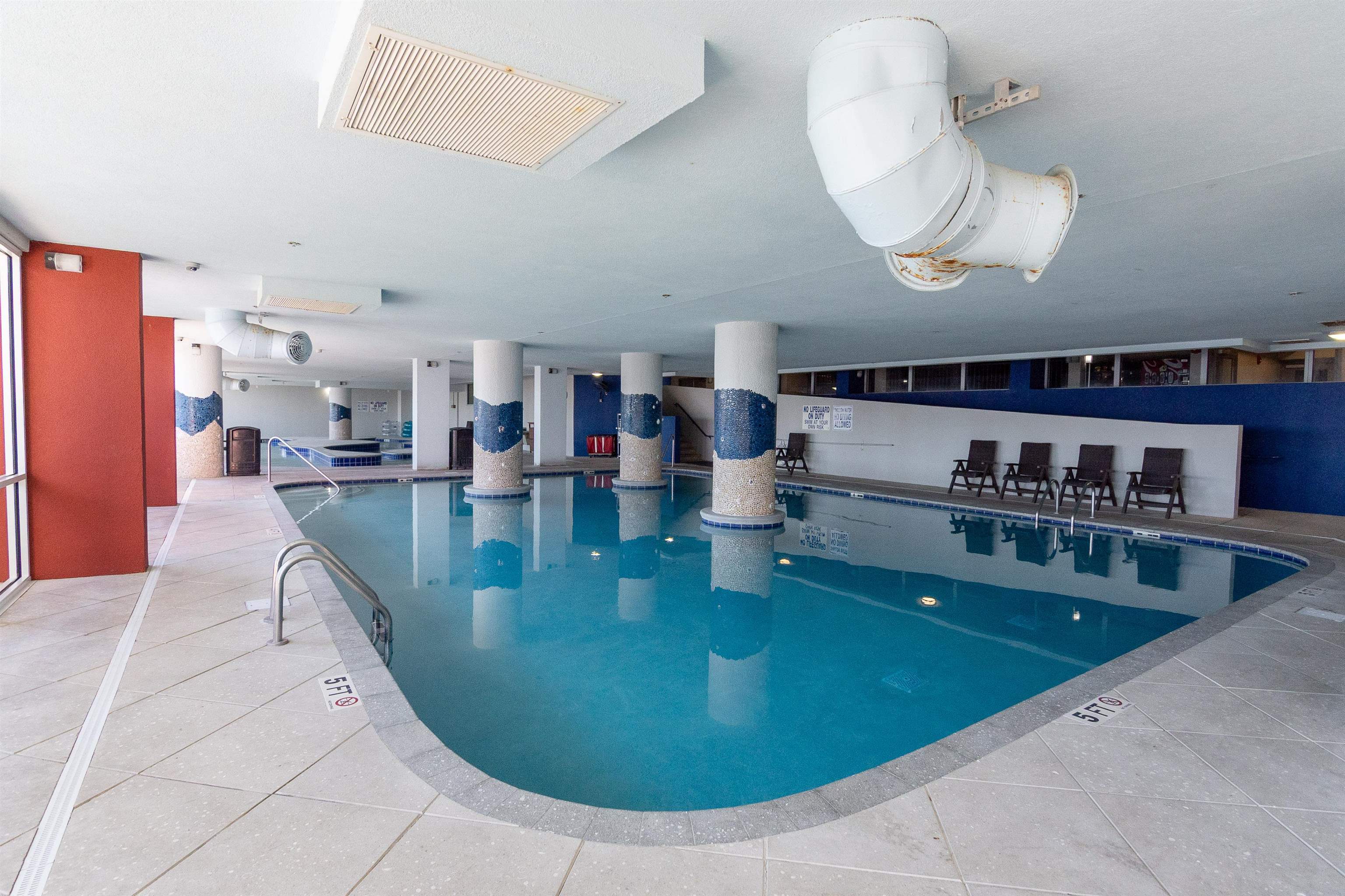 Indoor pool with tiled columns, blue water, and lounge chairs along the deck.