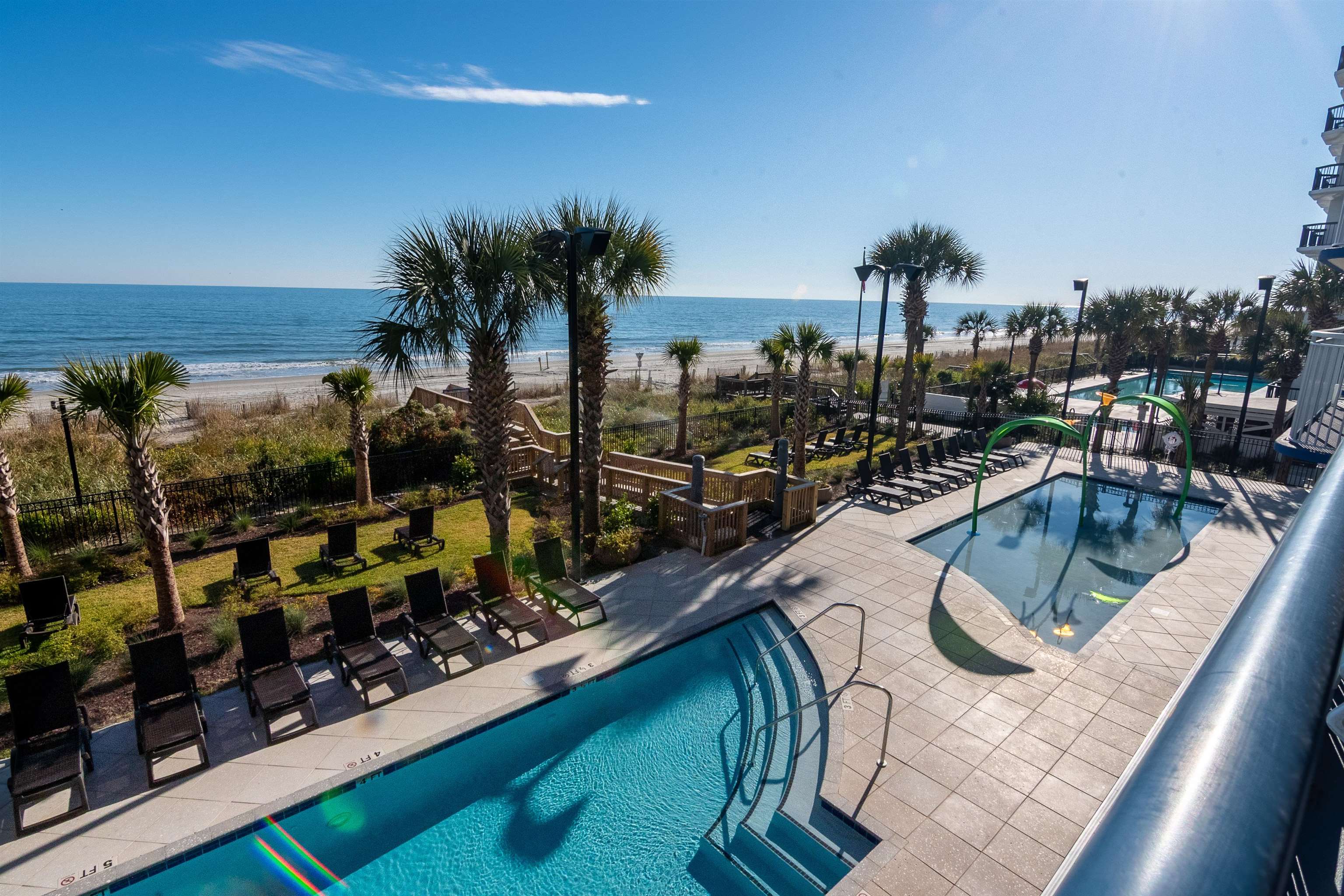 Oceanfront pool deck with lounge chairs and palm trees overlooking the beach and ocean.