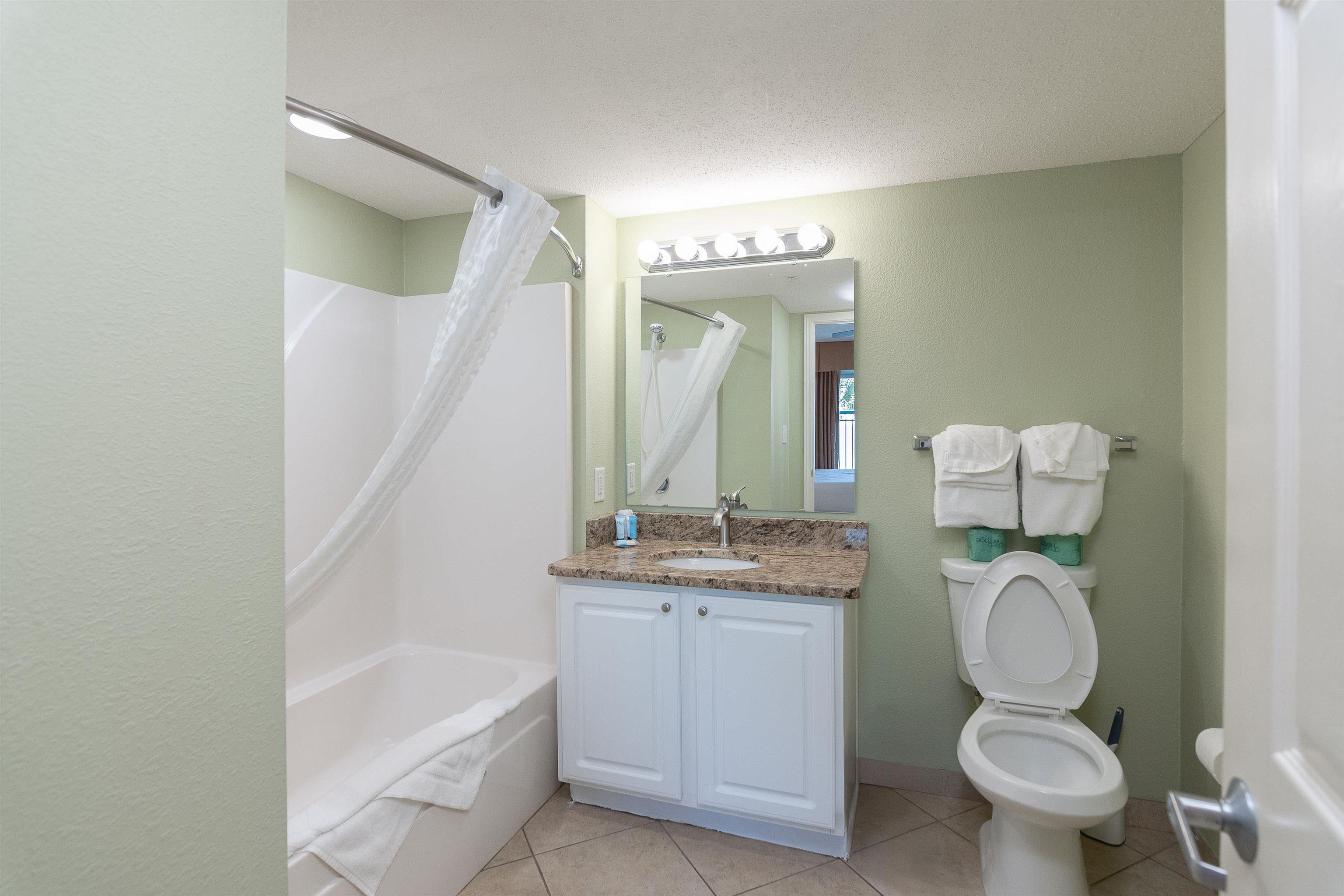 Bathroom with a white tub, stone-counter vanity, and toilet beneath folded towels.