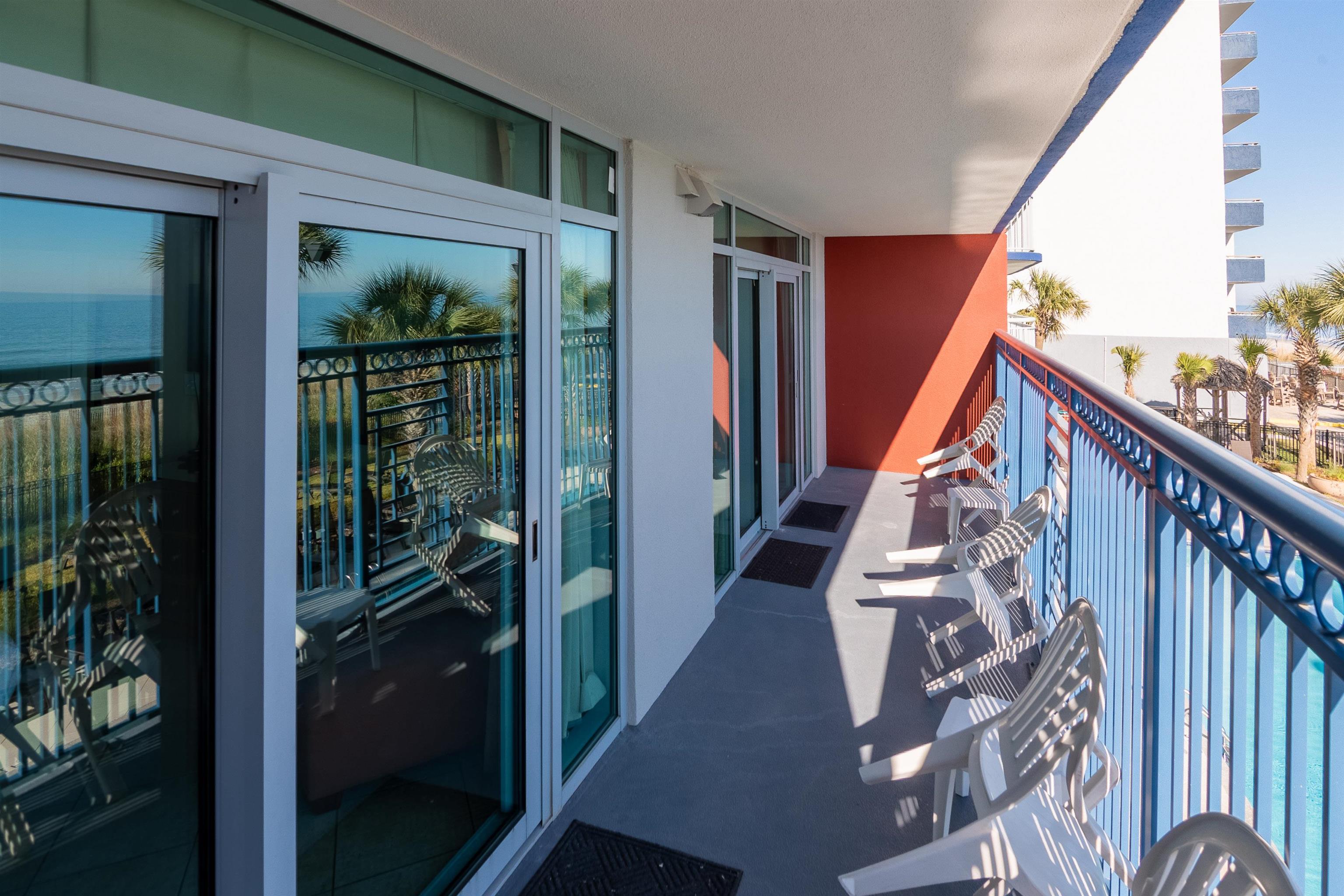 Oceanfront condo balcony with white lounge chairs, glass doors, and ocean views.