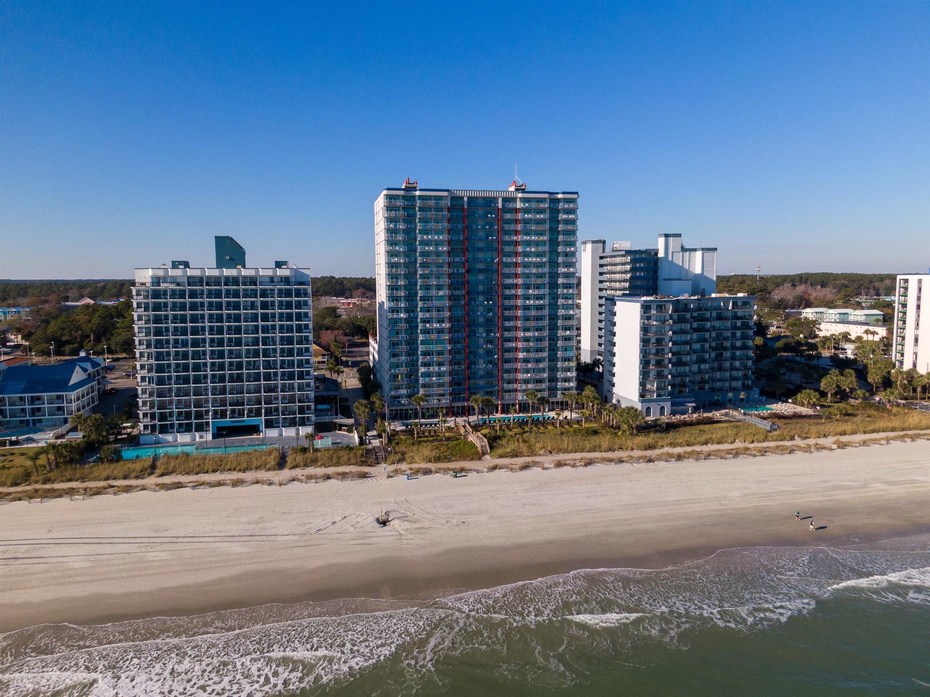 Beachfront condominiums with balconies beside a wide sandy beach and ocean waves.