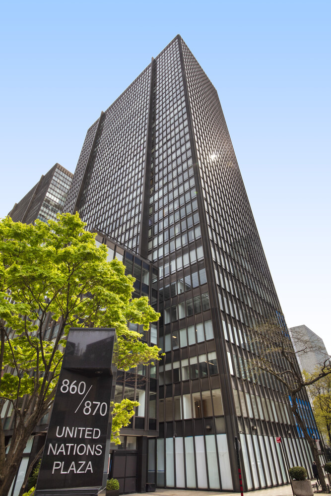 860 United Nations Plaza tower with its street-level address sign and leafy trees.