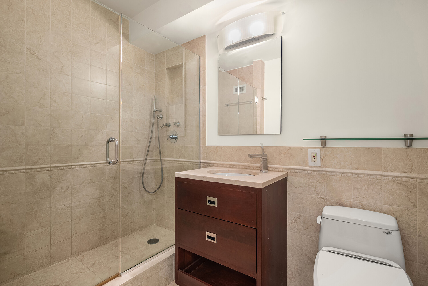Bathroom with a glass-enclosed shower, beige stone tile, and dark wood vanity.