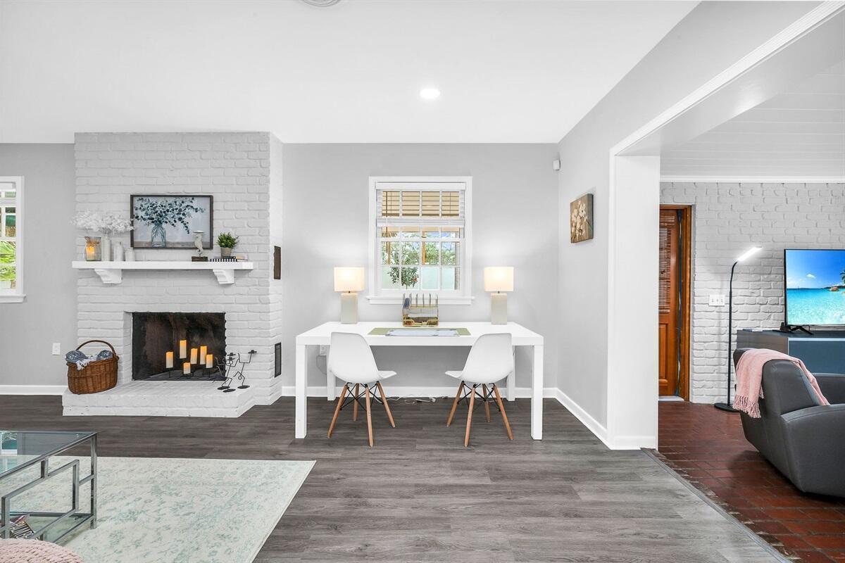 Bright living and dining area with white brick fireplace, white table, and adjacent sitting room.