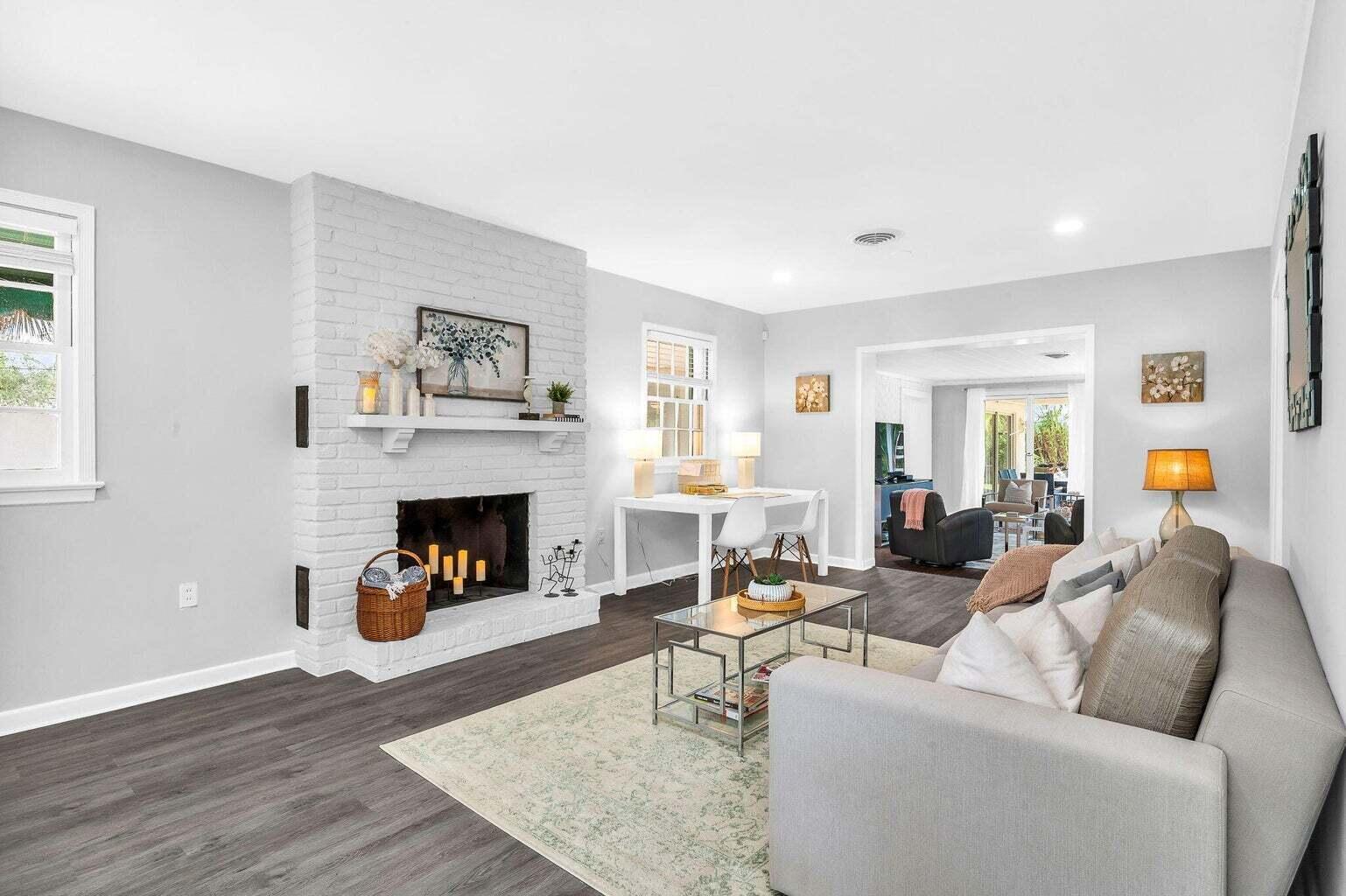 Furnished living room with a white brick fireplace, gray sectional, and dark wood-look floors.