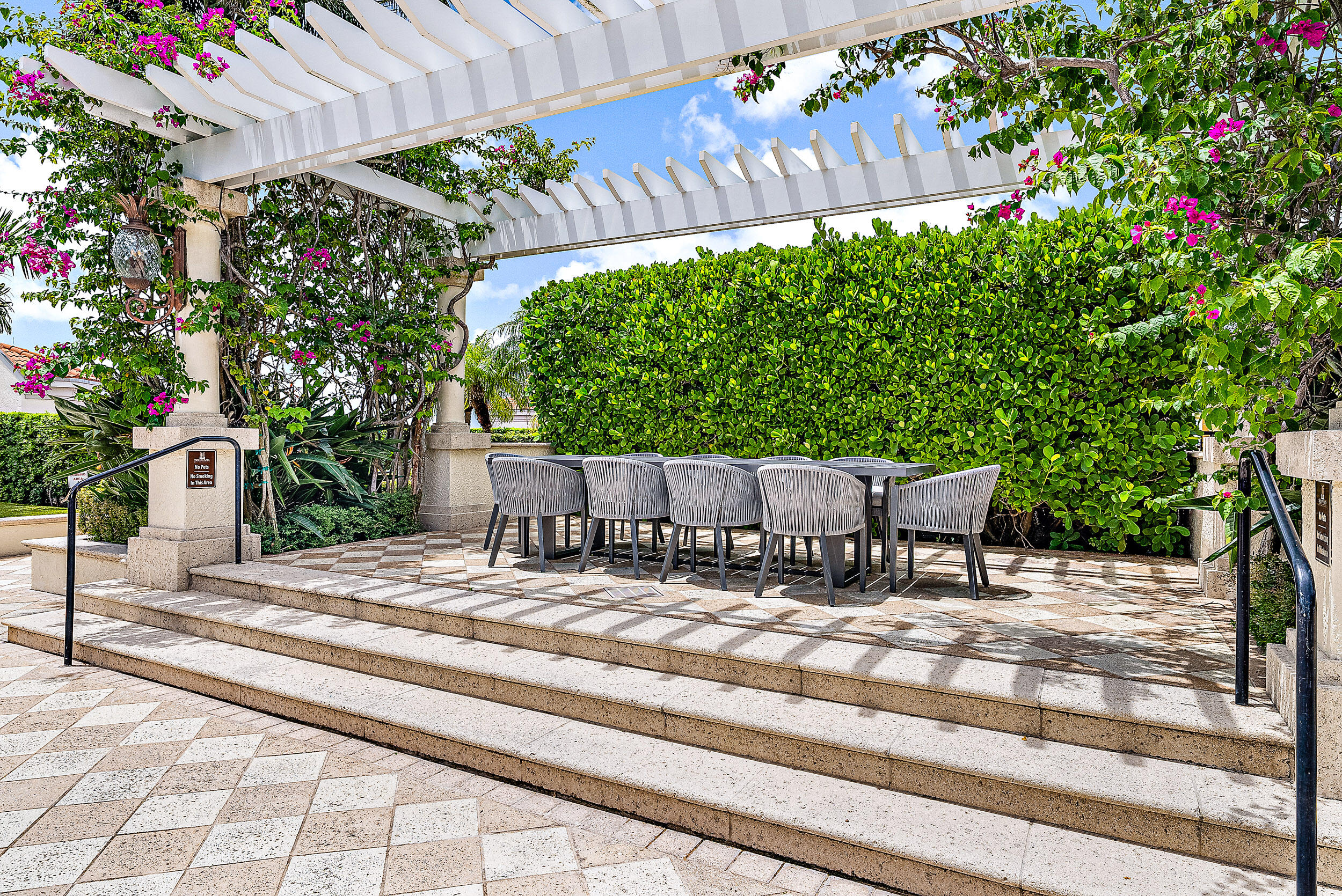 Outdoor patio with a pergola-covered dining table, tiled steps, and tropical landscaping.
