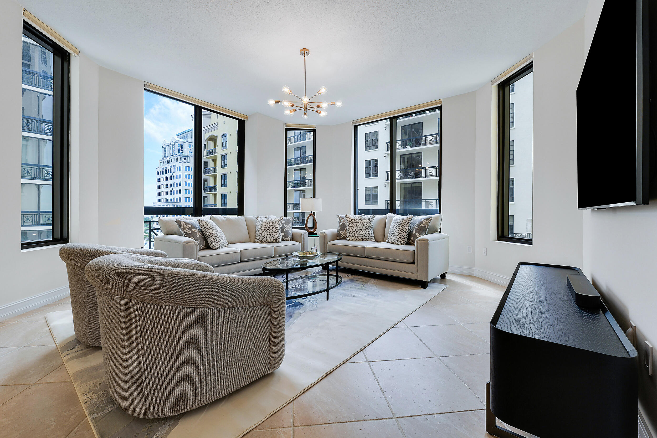 Furnished high-rise living room with large windows overlooking neighboring buildings.