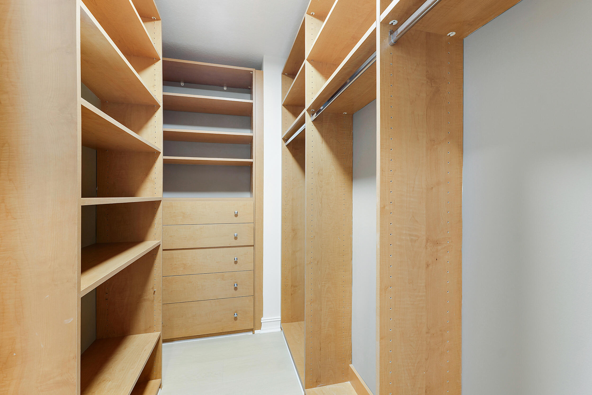 Walk-in closet with light wood built-in shelves, drawers, and hanging rods.
