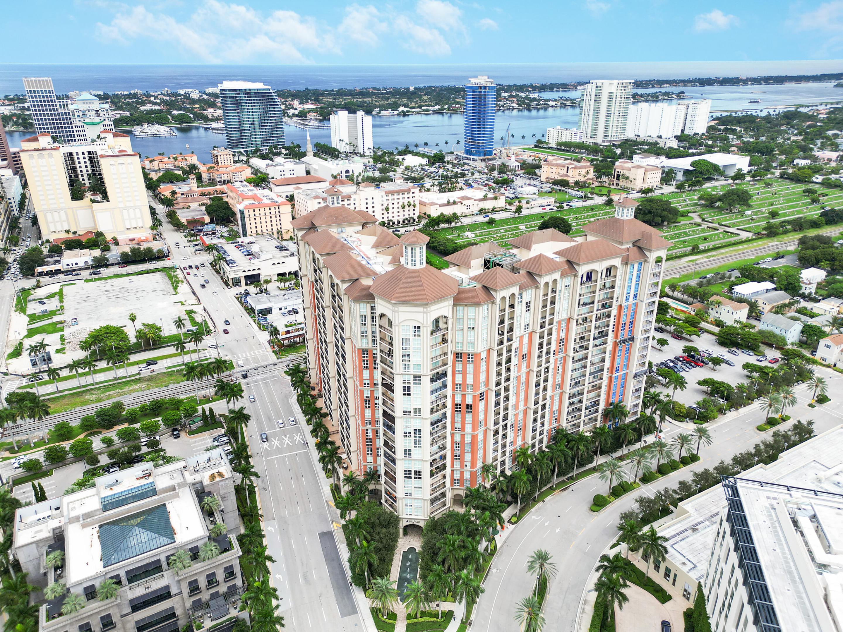 Aerial view of a coral-accented high-rise condominium amid downtown streets, with waterfront and skyline beyond.