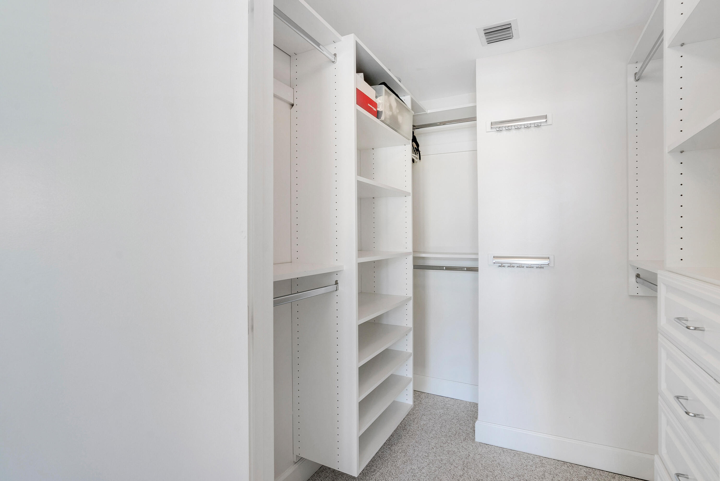 Walk-in closet with white built-in shelves, hanging rods, and carpeted floor.