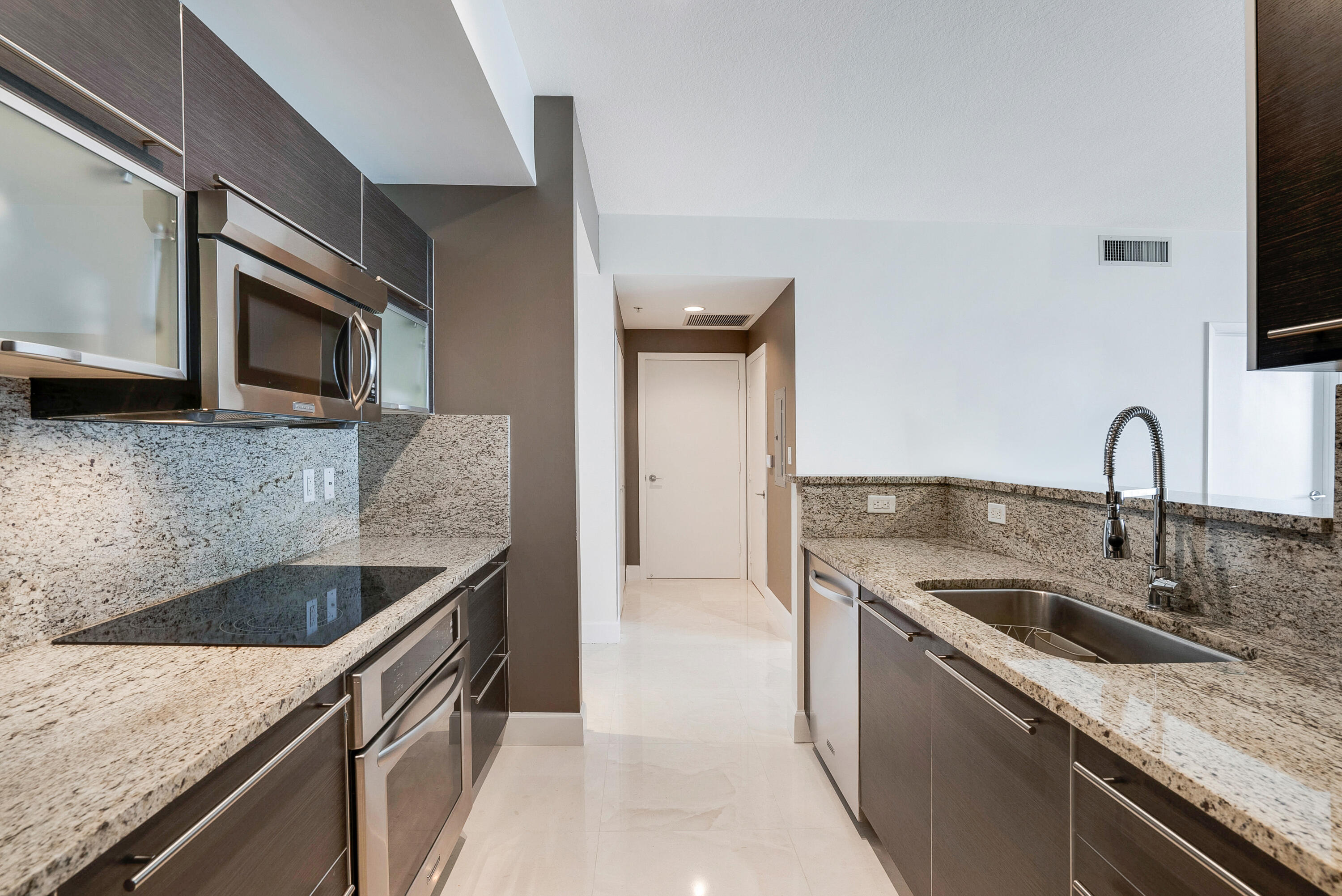 Modern kitchen with granite counters, dark cabinetry, stainless appliances, and a deep sink with a coil faucet.