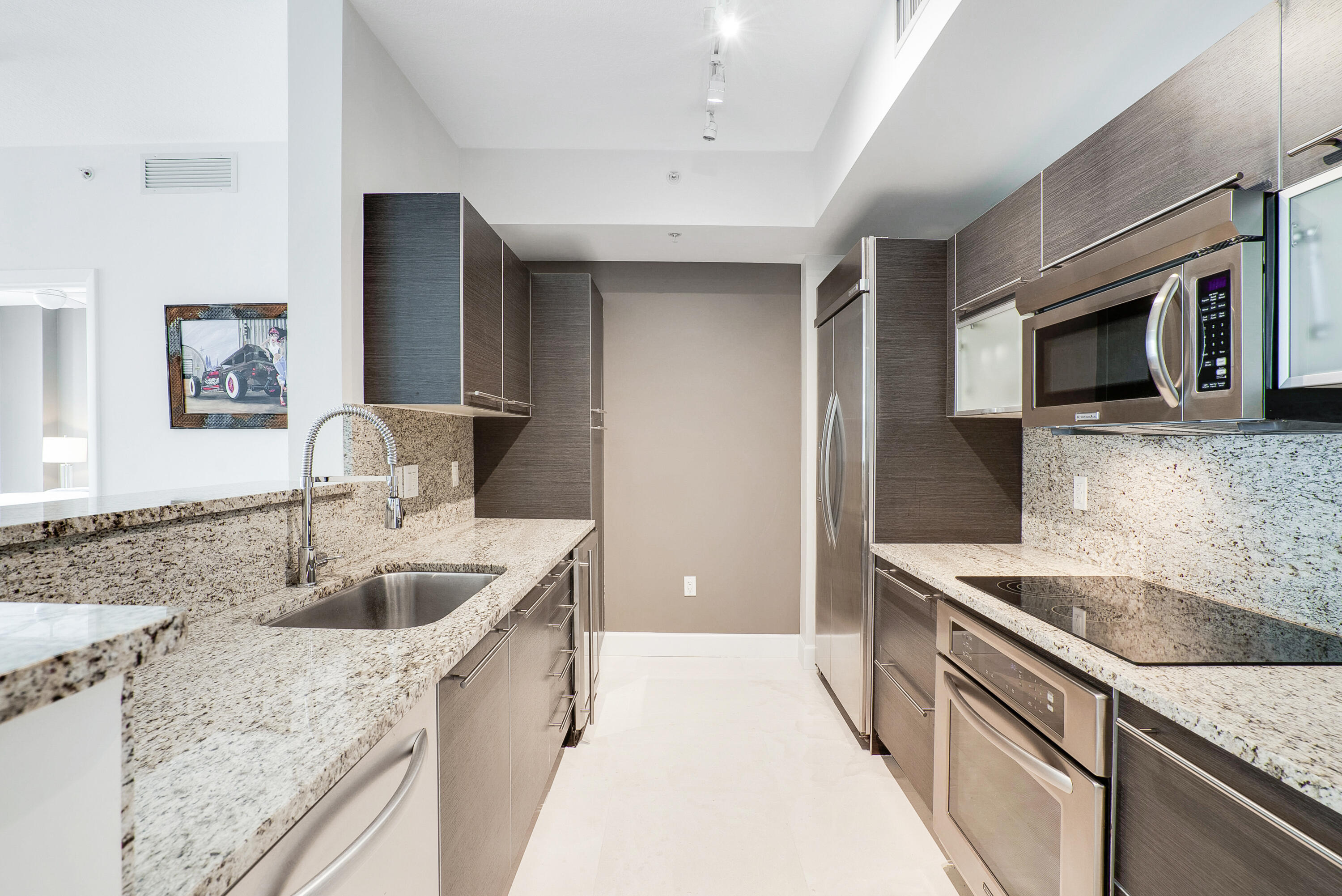 Modern galley kitchen with dark cabinetry, granite counters, and stainless steel appliances.