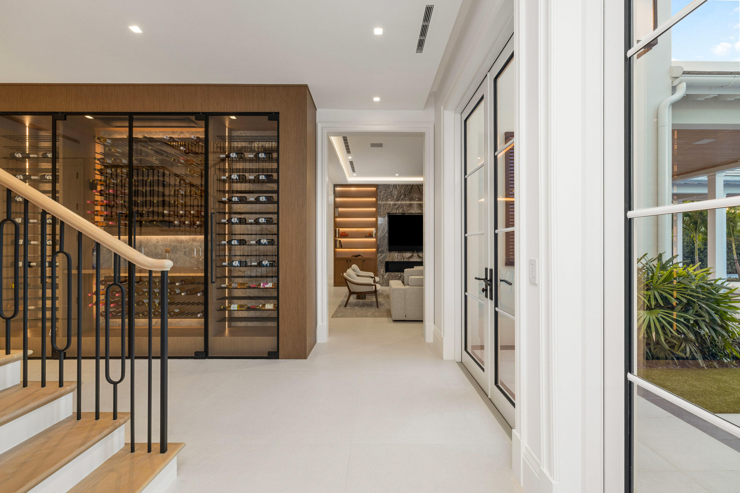 Hallway with a glass-fronted wine cellar, wood staircase, and views into a furnished living room.