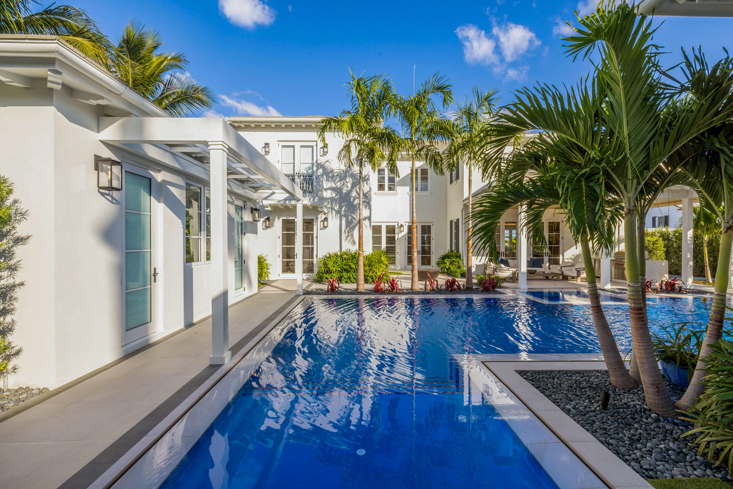 White modern home surrounding a blue pool, framed by palms and a covered patio.