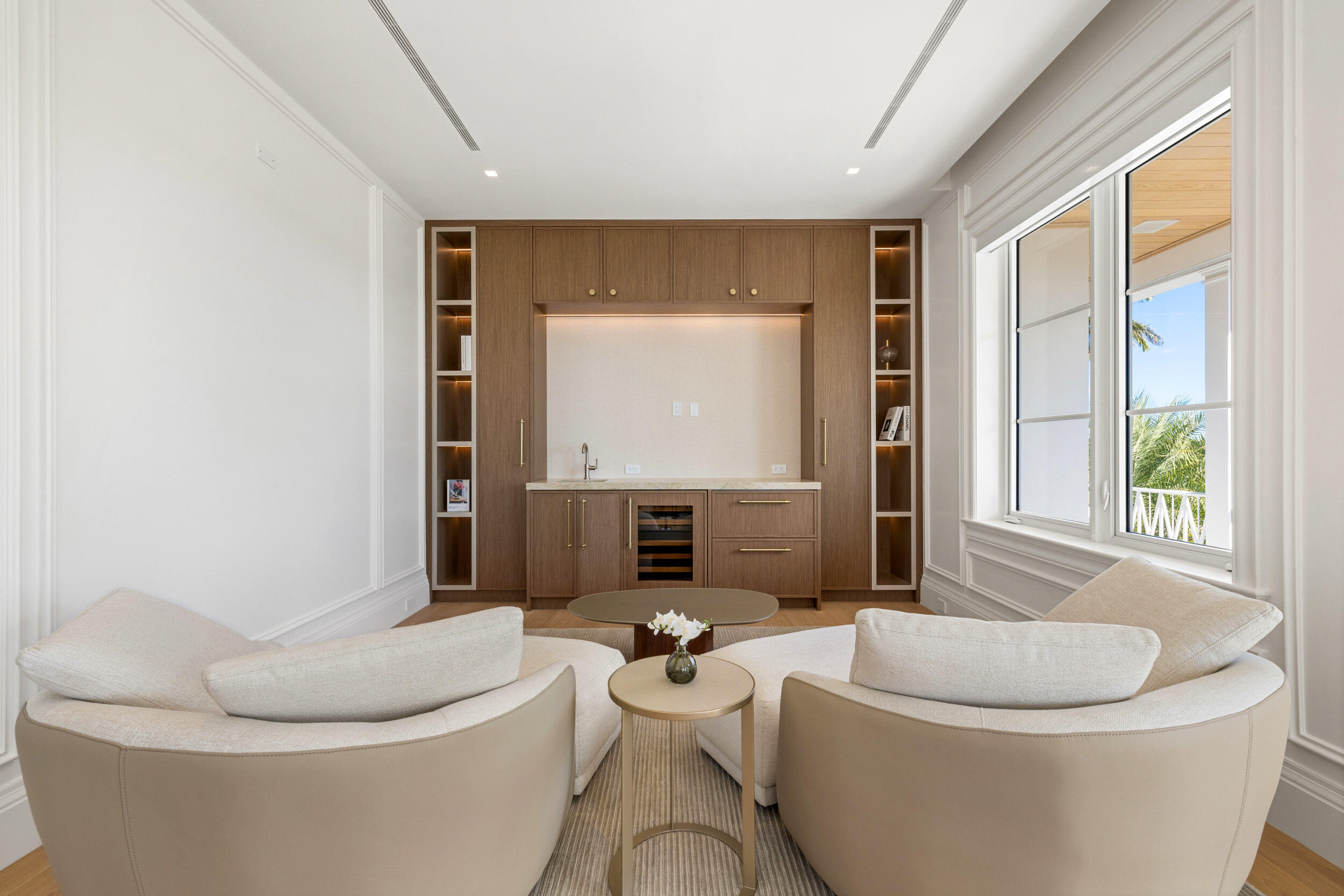 Furnished sitting room with curved cream sofas, walnut built-ins, a wine fridge, and large windows.
