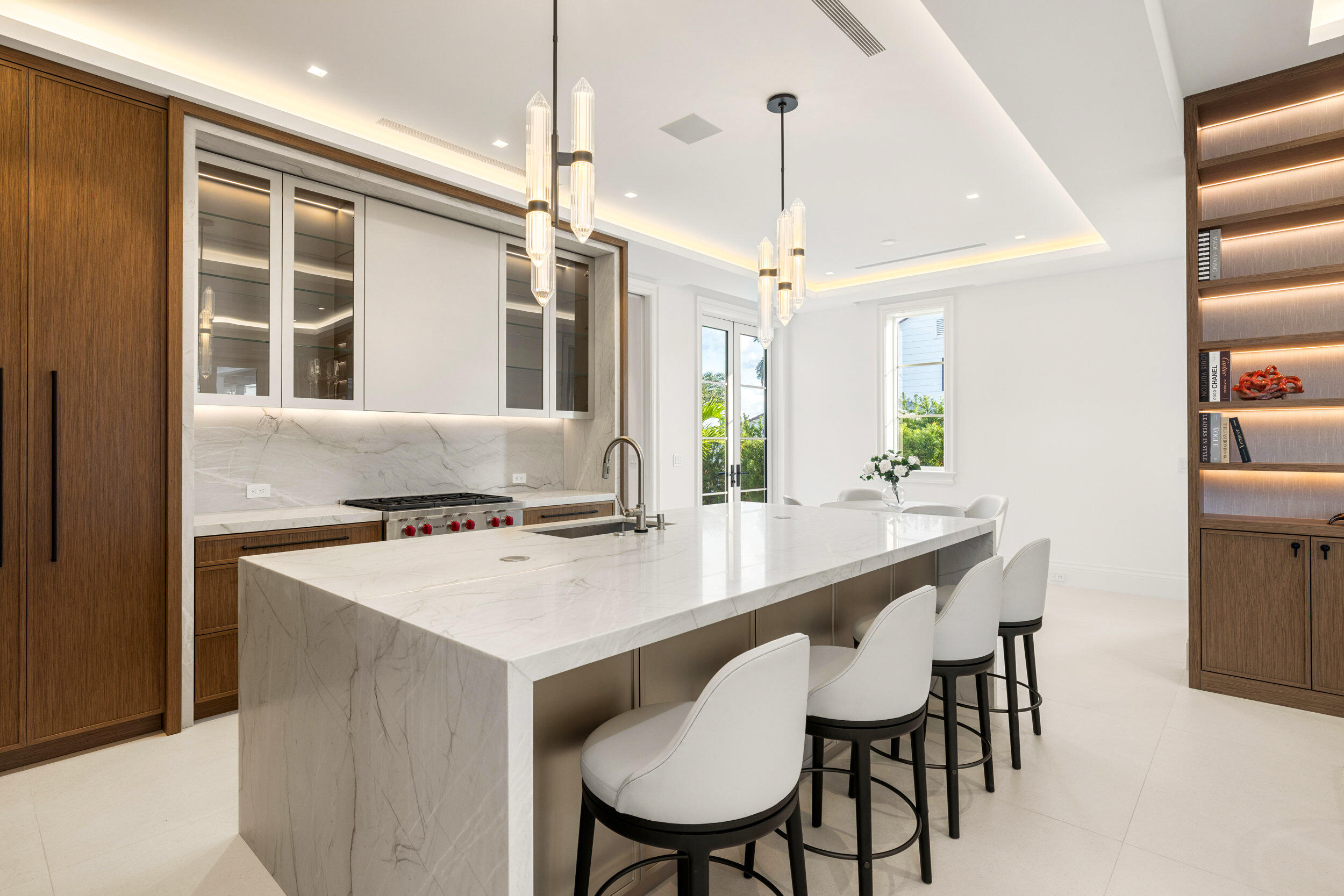 Modern kitchen with a large marble waterfall island, white stools, and dark wood cabinetry.