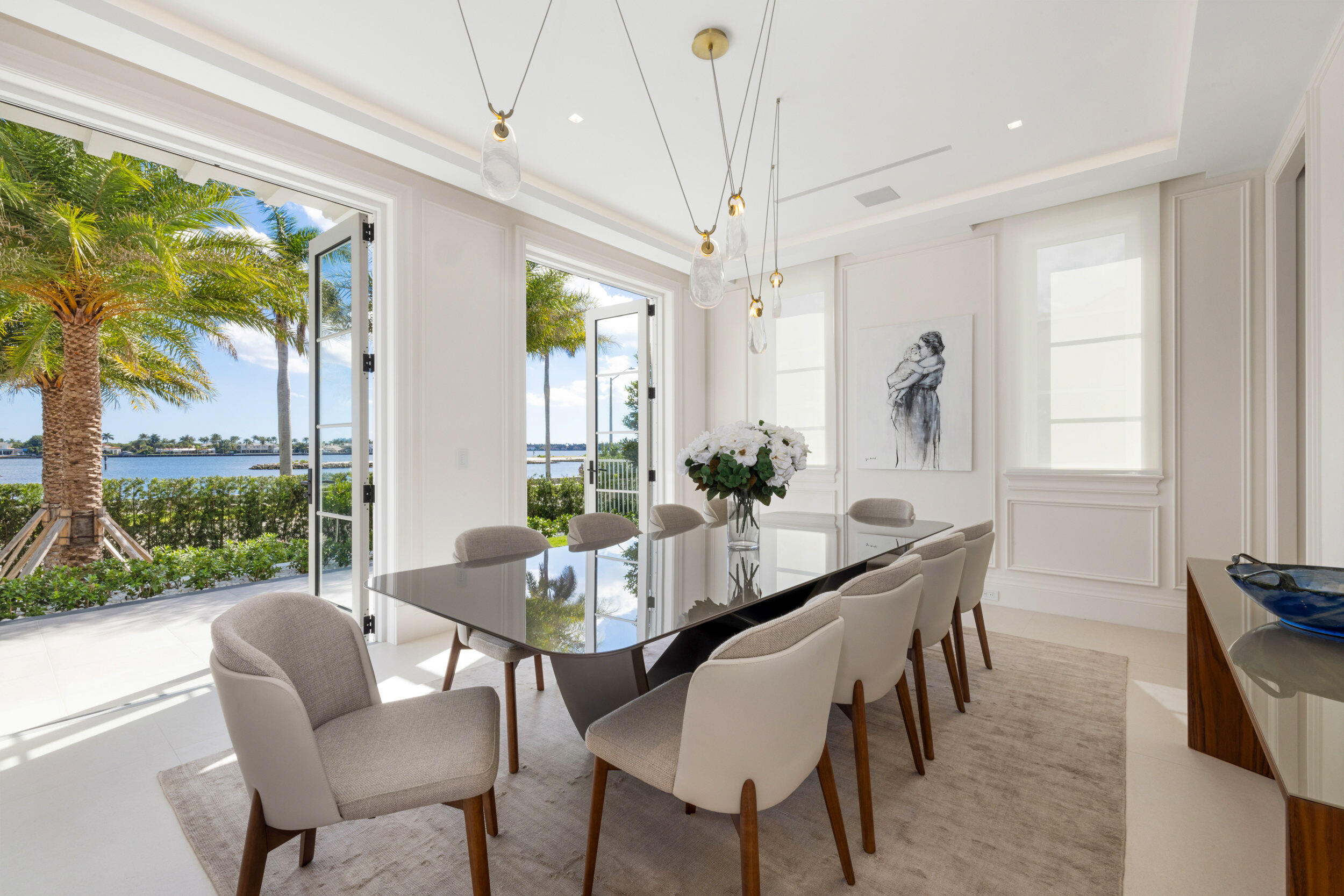 Dining room with a glossy table and chairs overlooking the water through open glass doors.